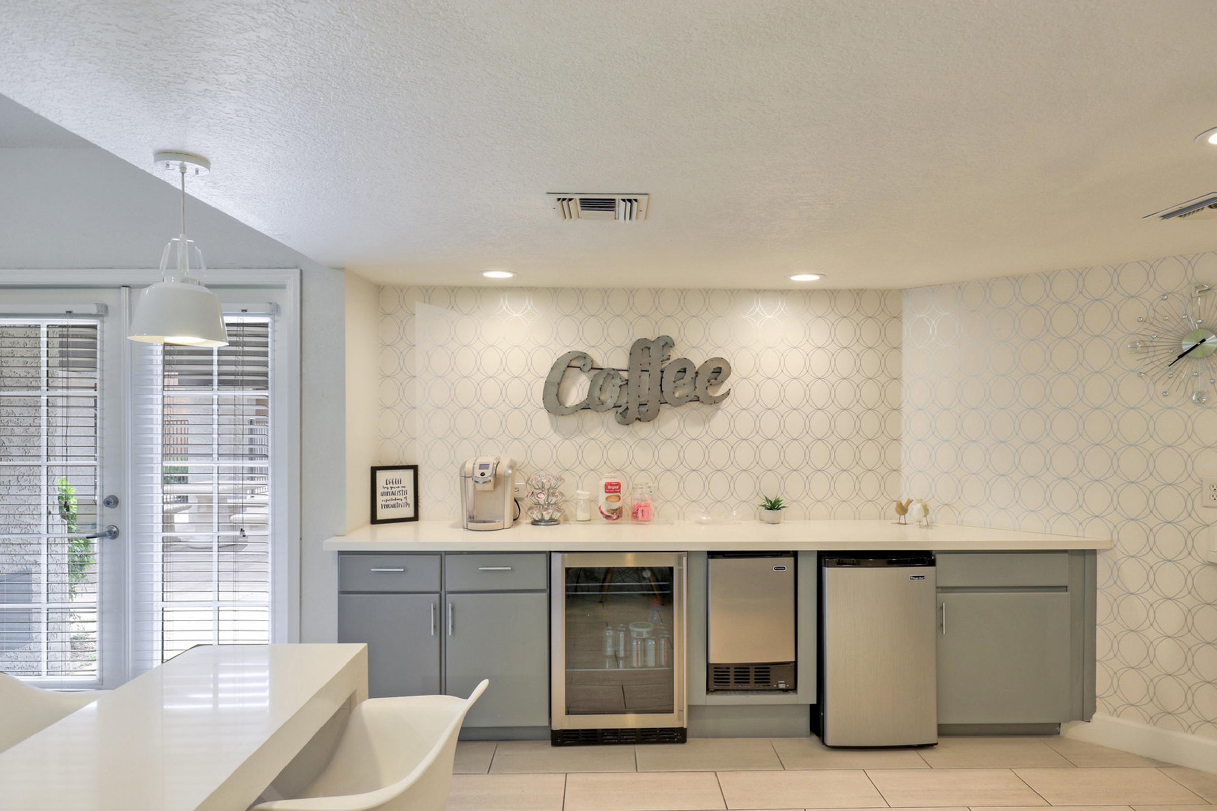 Modern kitchen with a light color scheme, featuring a coffee station with a coffee maker, a small fridge, and decorative elements.