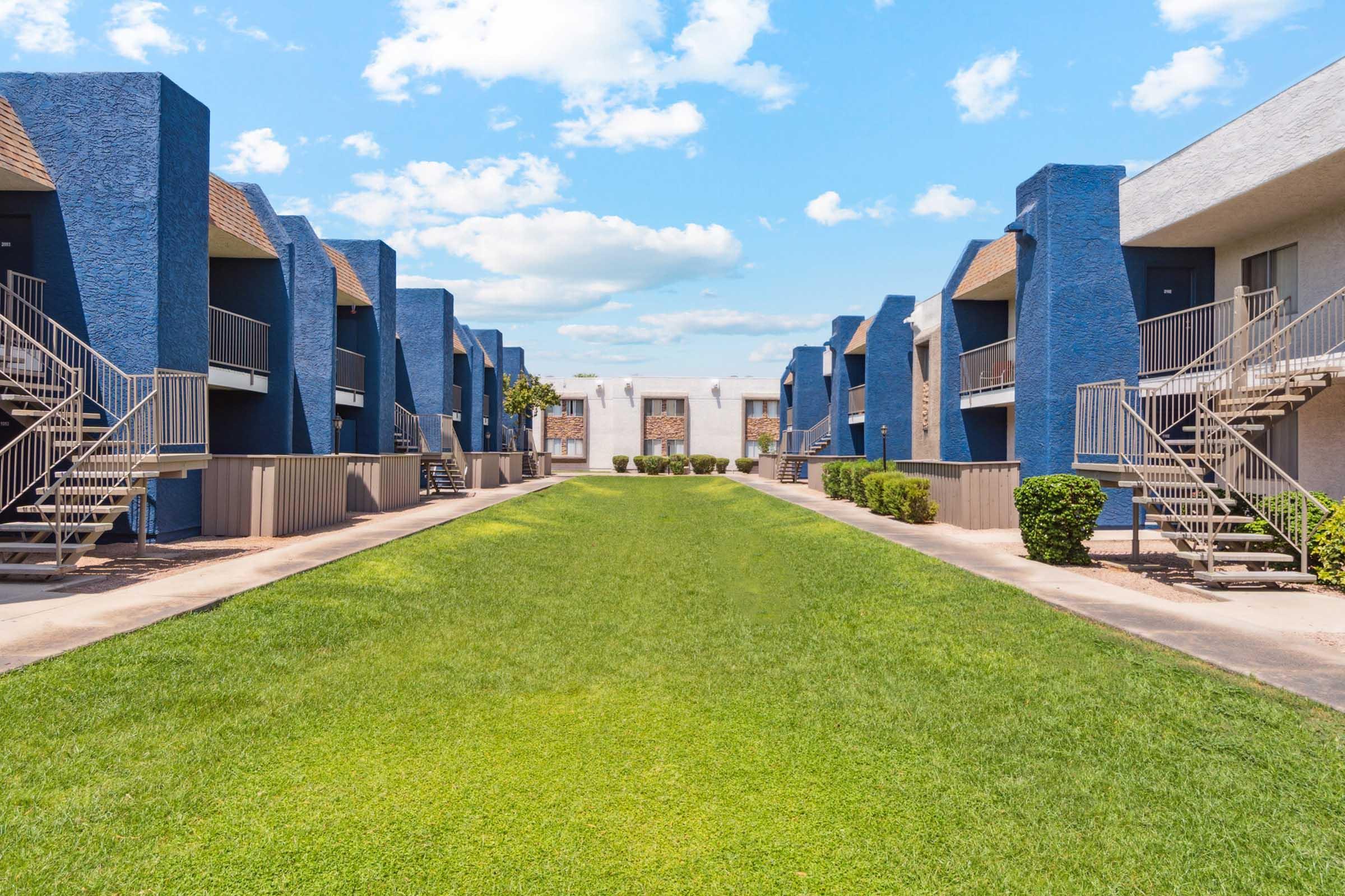 View of a green courtyard flanked by two rows of blue and beige apartment buildings.