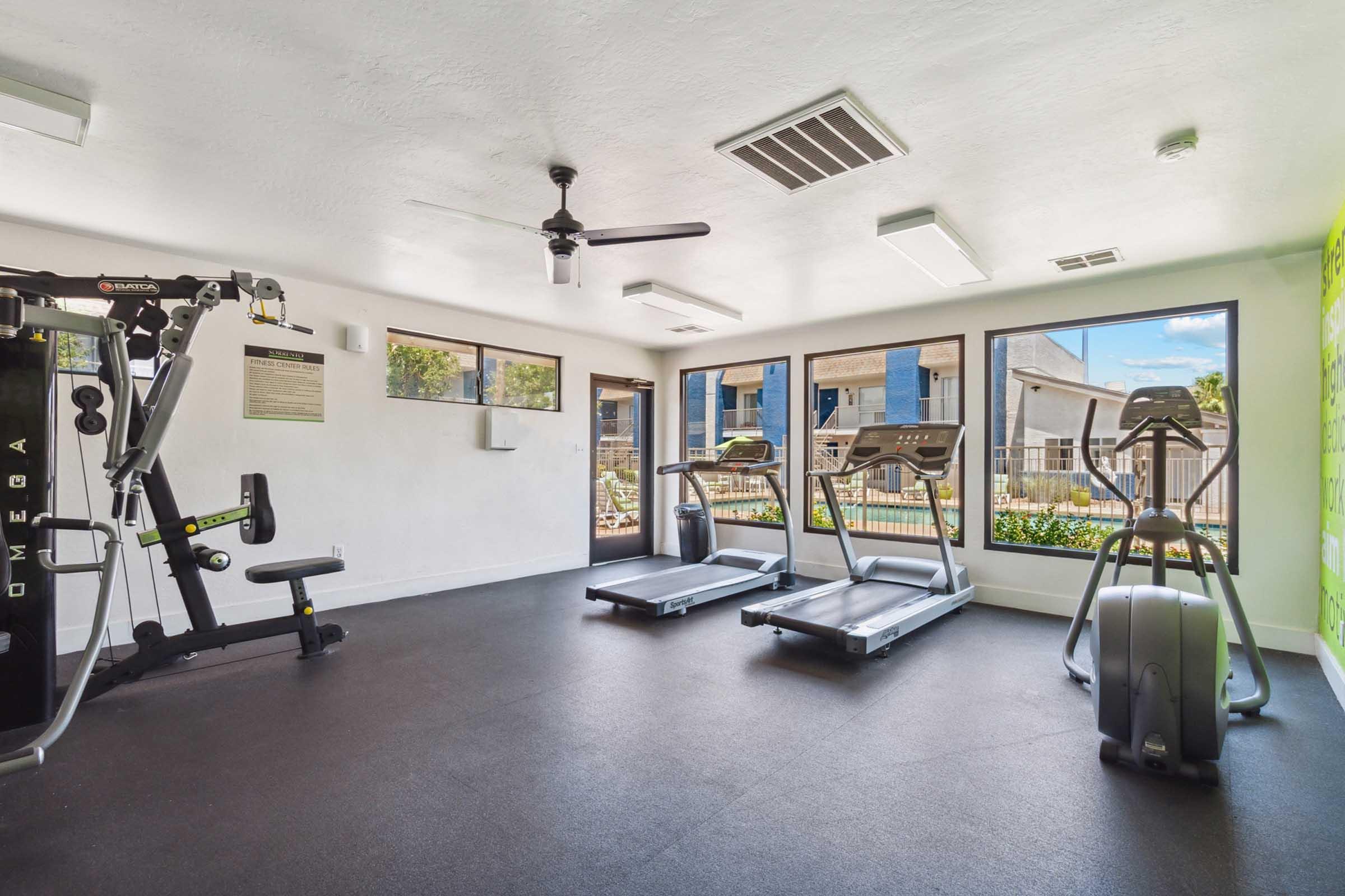 A modern gym interior featuring two treadmills and an elliptical machine arranged along large windows.