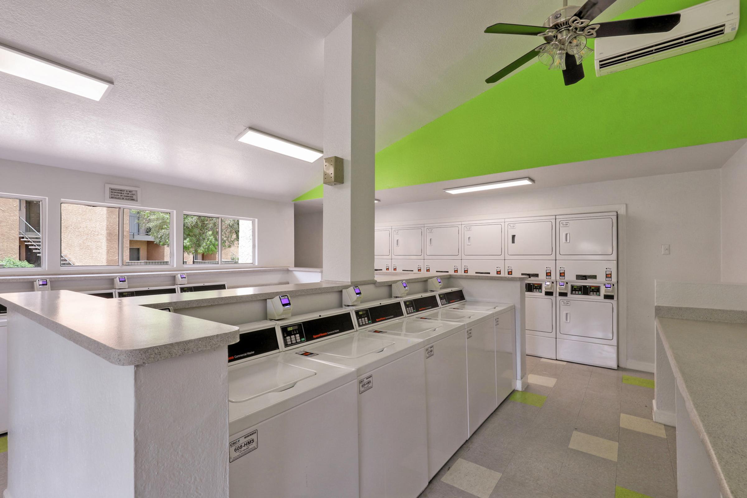 A modern laundry room with multiple white washing machines and dryers arranged in rows.
