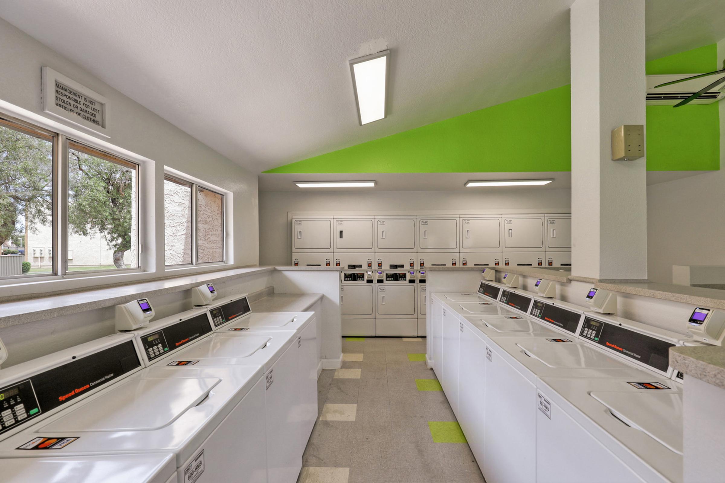 A clean, bright laundry room featuring multiple washing machines and dryers lined up against the walls.
