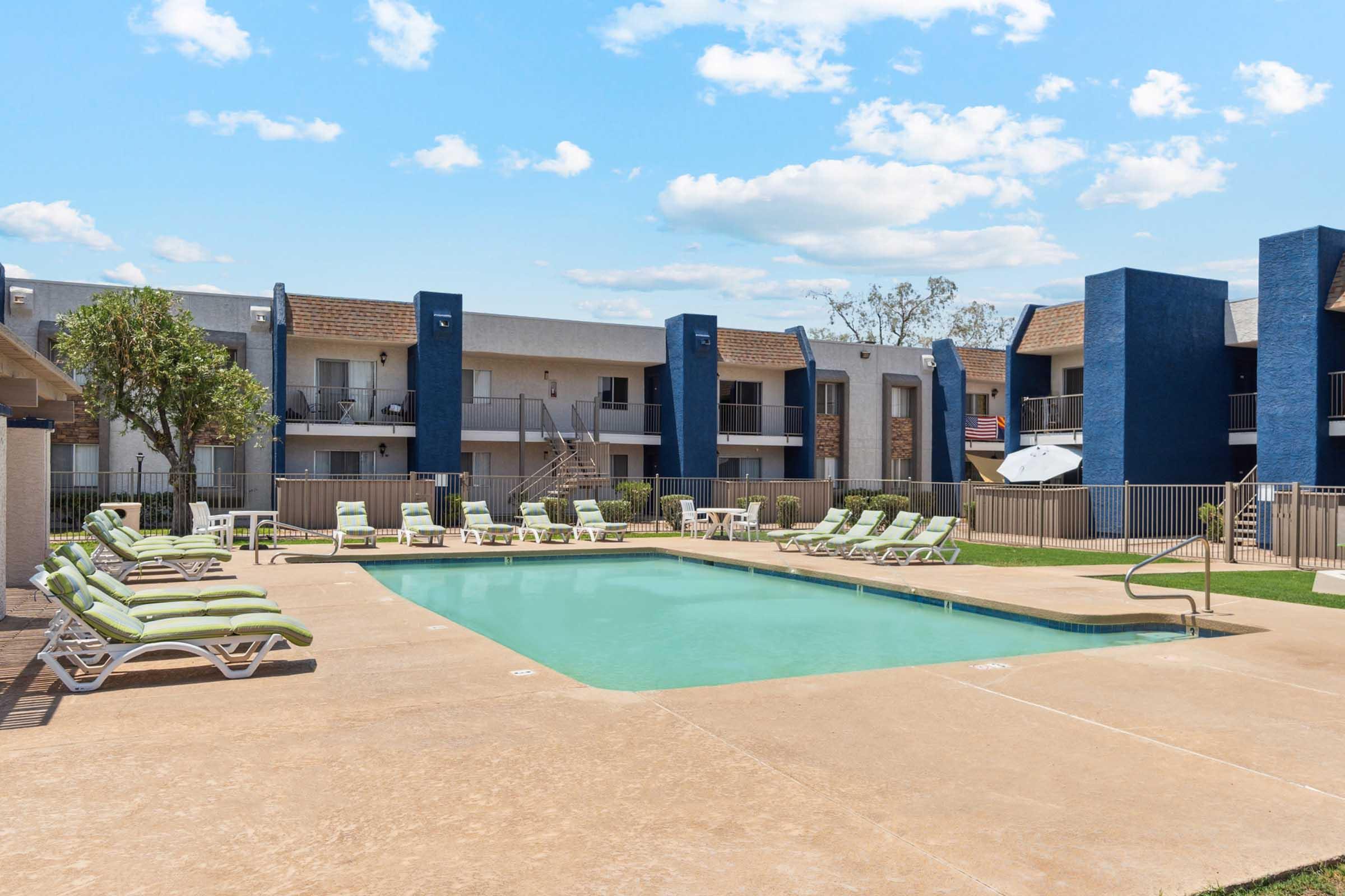 A serene outdoor swimming pool surrounded by lounge chairs, set within a well-maintained apartment complex.