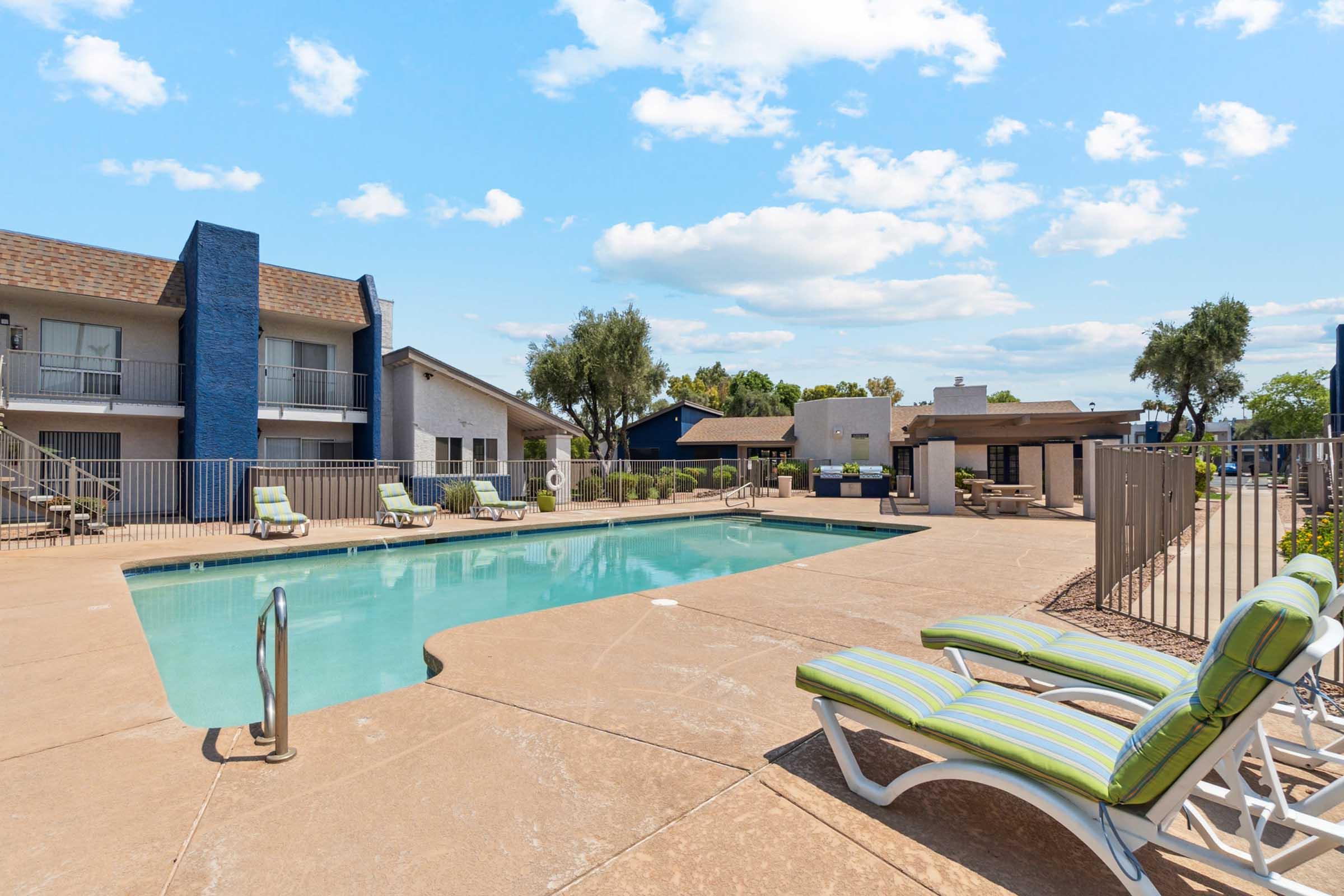 A sunny outdoor pool area with a clear blue water pool surrounded by lounge chairs.