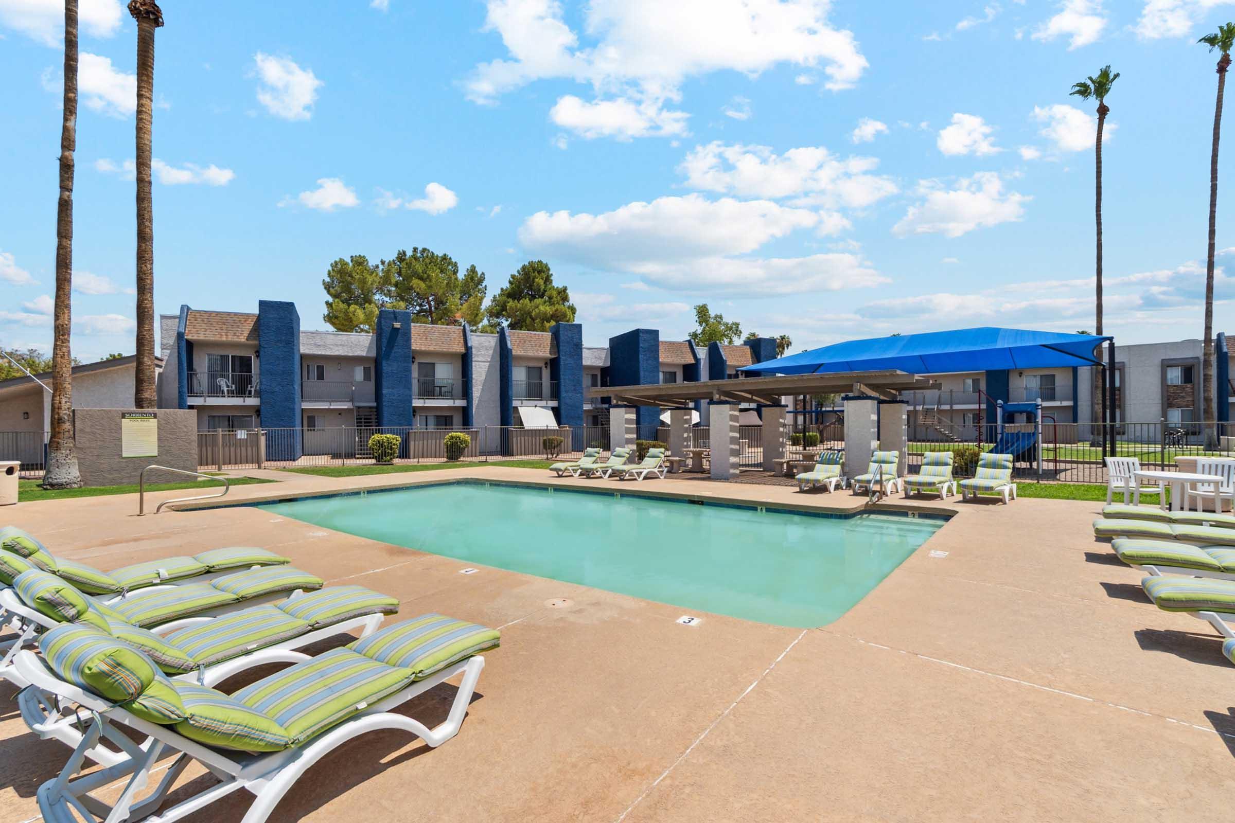 A clear swimming pool surrounded by lounge chairs with green and white stripes.
