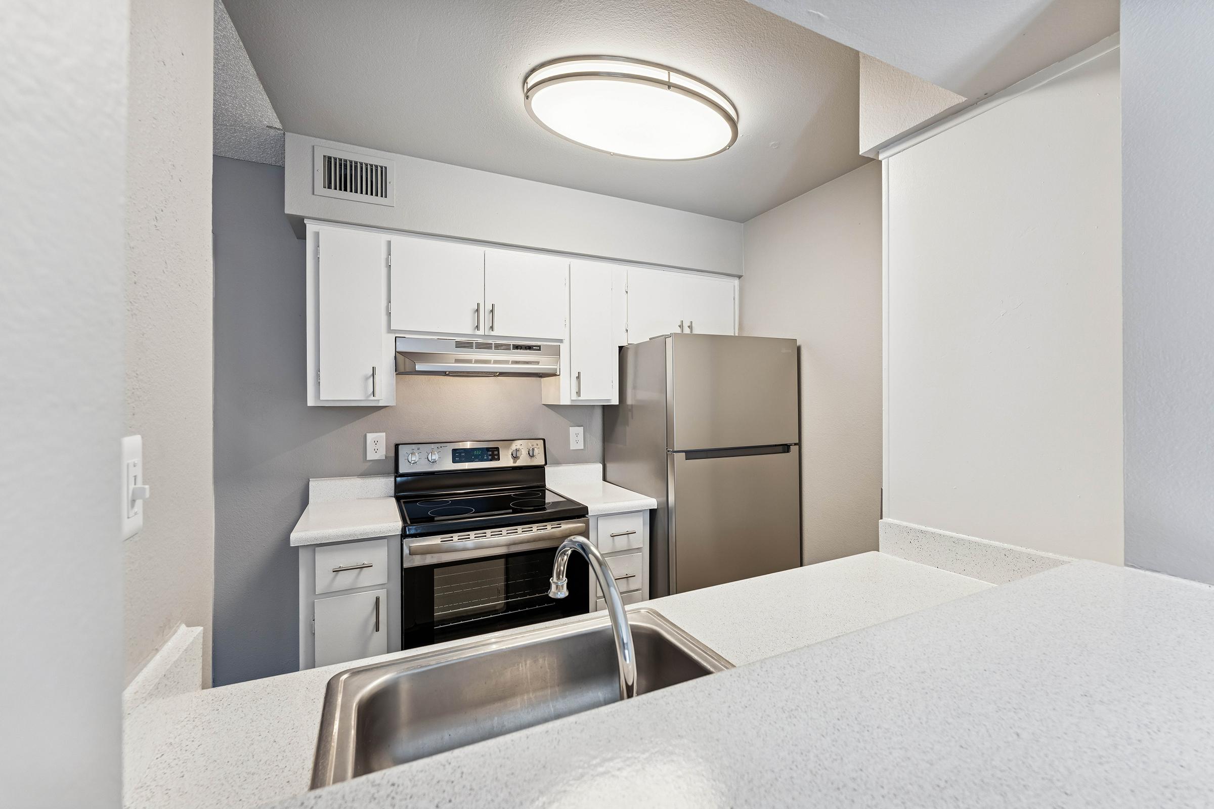 Modern kitchen featuring white cabinetry, stainless steel appliances including an oven and refrigerator, and a spacious countertop. The room is well-lit with a circular ceiling light, showcasing a clean, contemporary design.