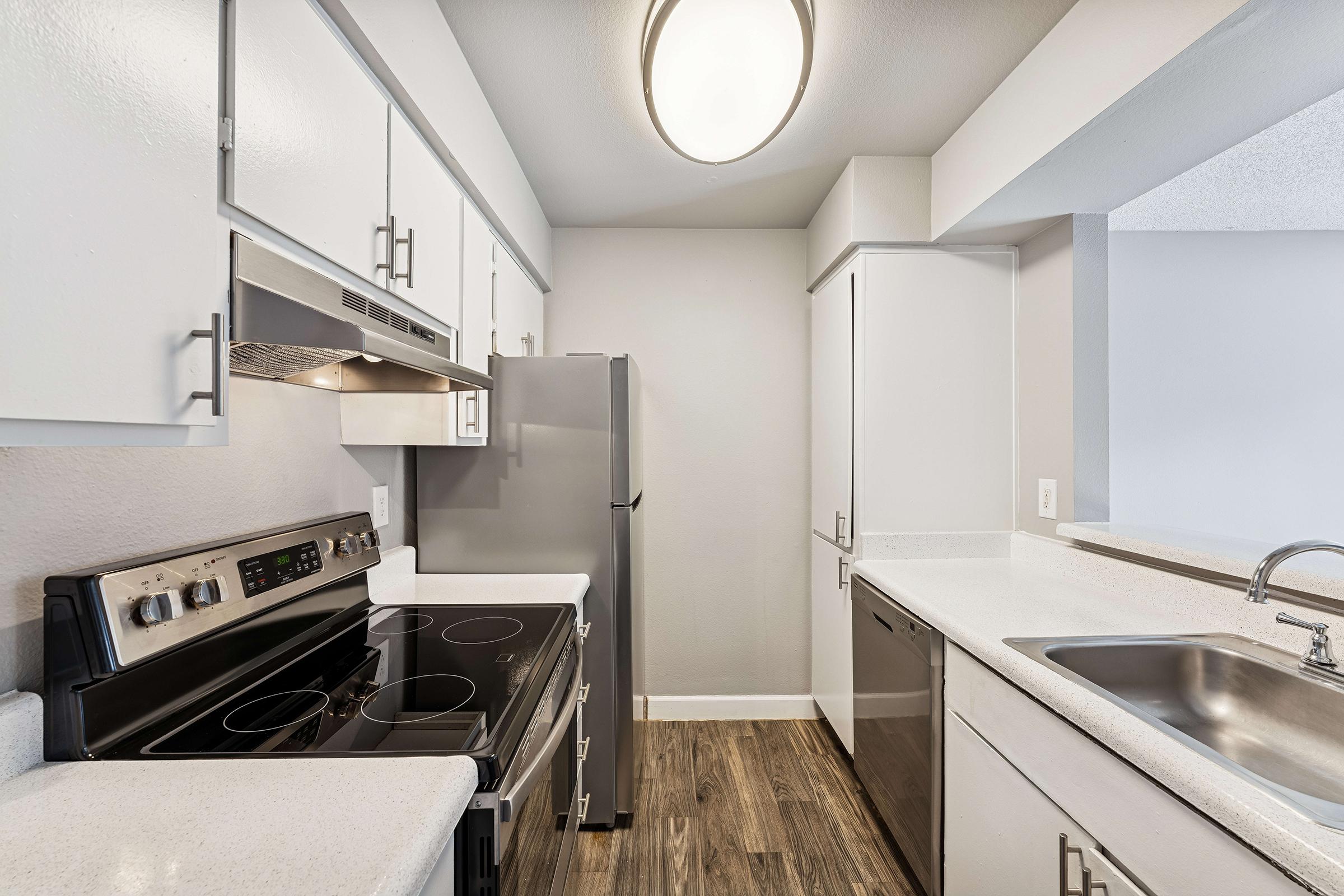Modern kitchen featuring white cabinets, stainless steel appliances including a refrigerator and stove, and a sleek countertop. The space is well-lit by a ceiling light, with a spacious layout that includes a double sink and ample counter space.