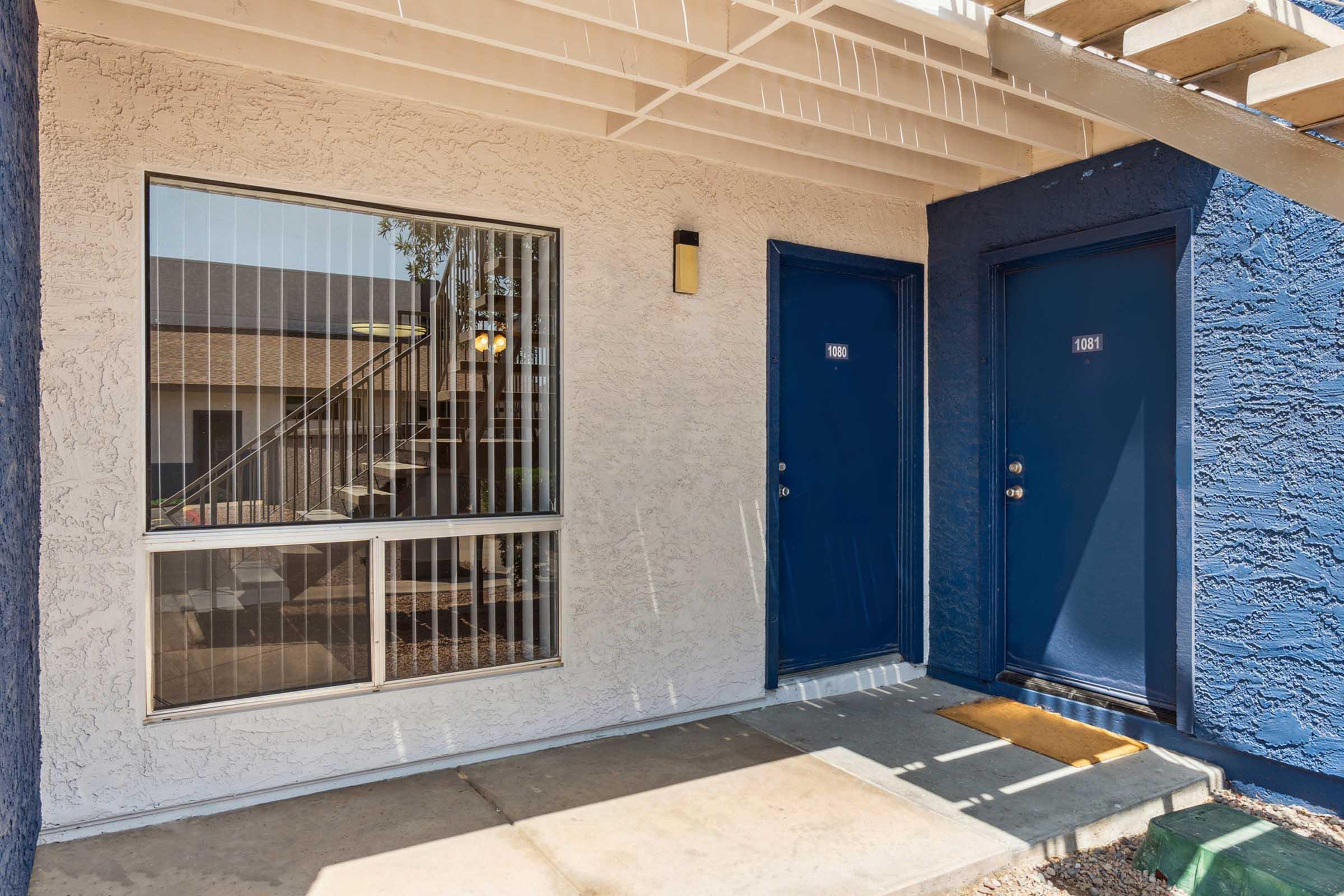 An exterior view of a multi-unit apartment building entrance featuring two blue doors