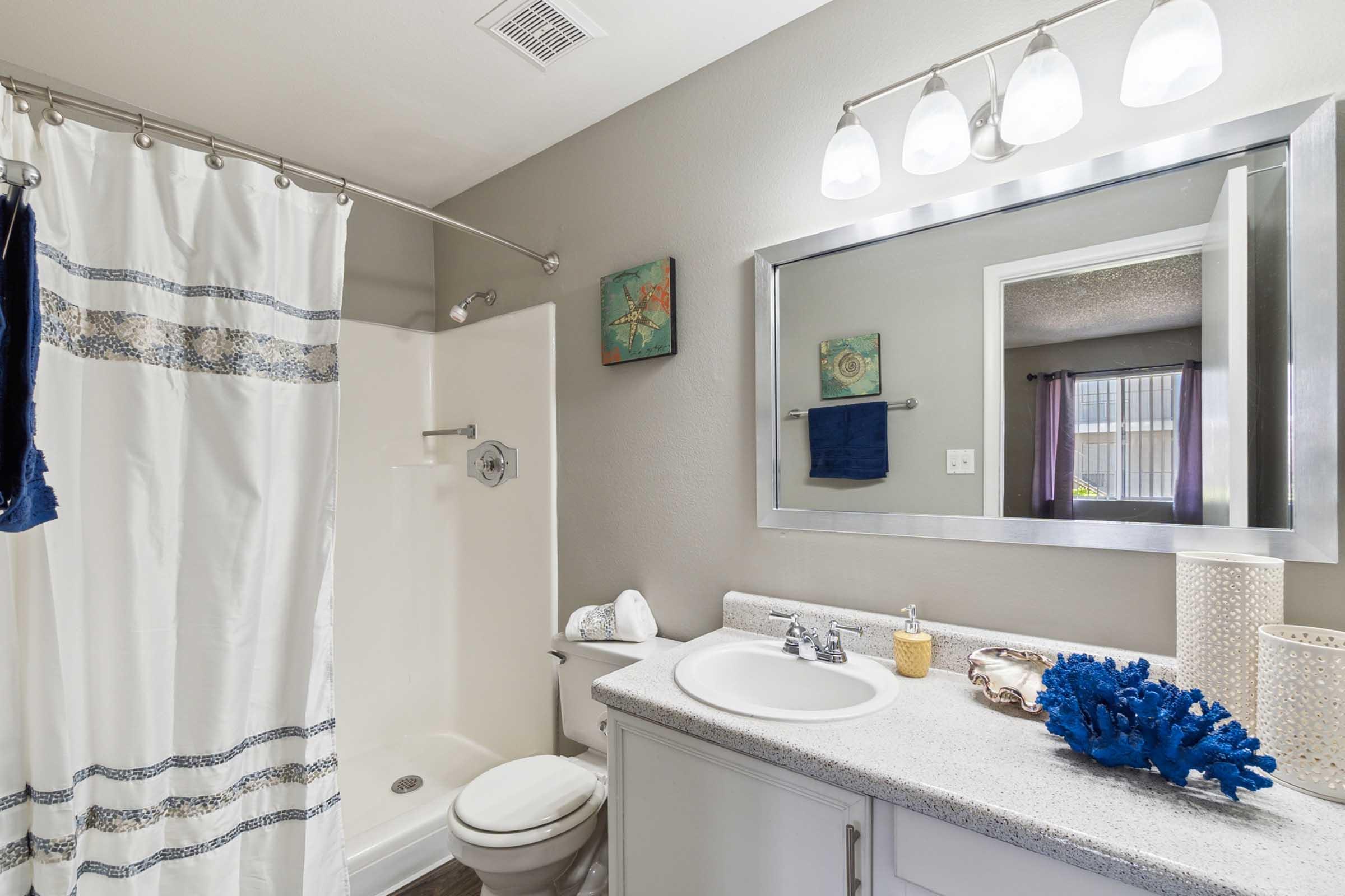 A modern bathroom featuring a shower with a white curtain, a toilet, and a sink with a countertop.