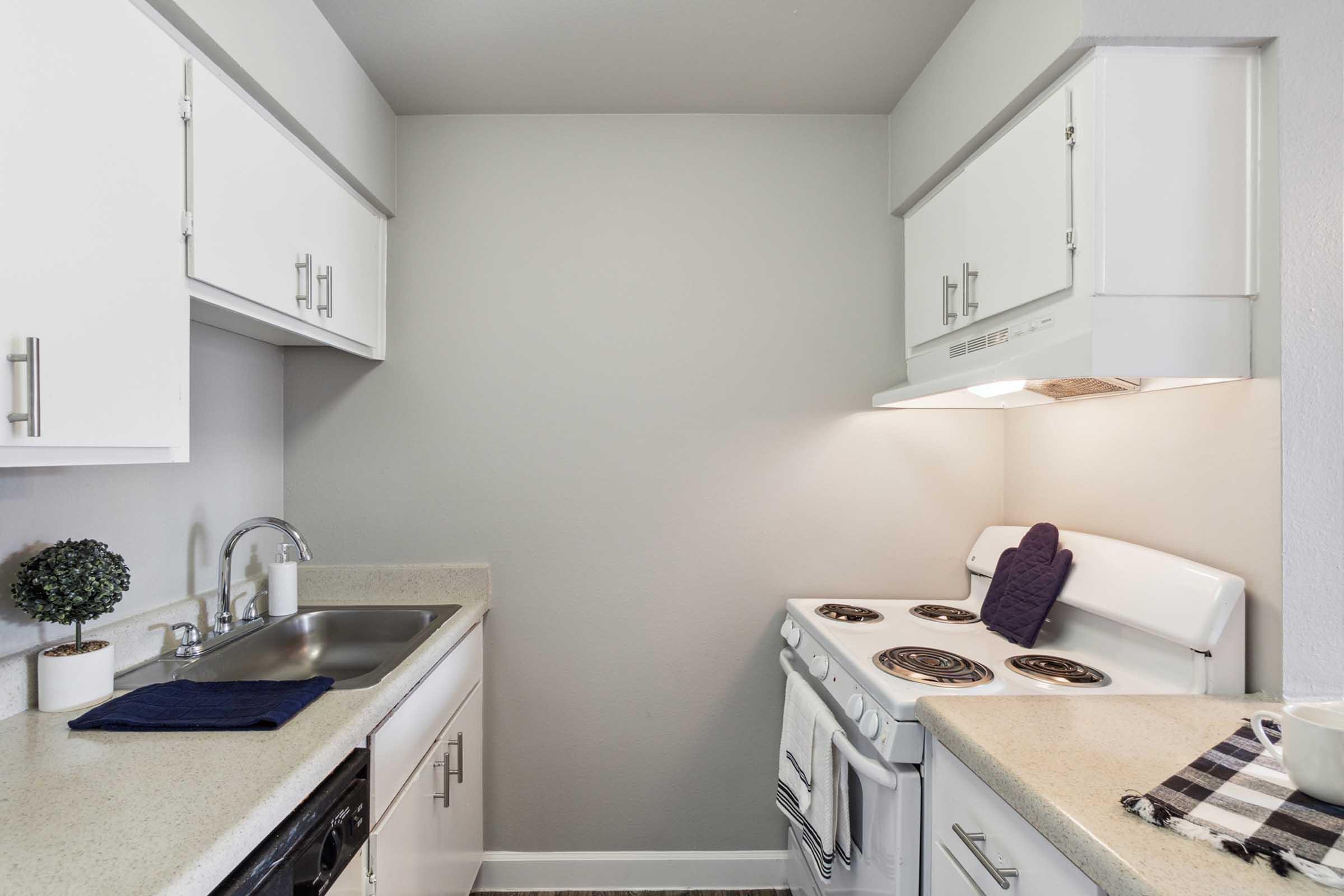 A compact kitchen featuring white cabinetry, a stainless steel sink, and a white stove with four burners.