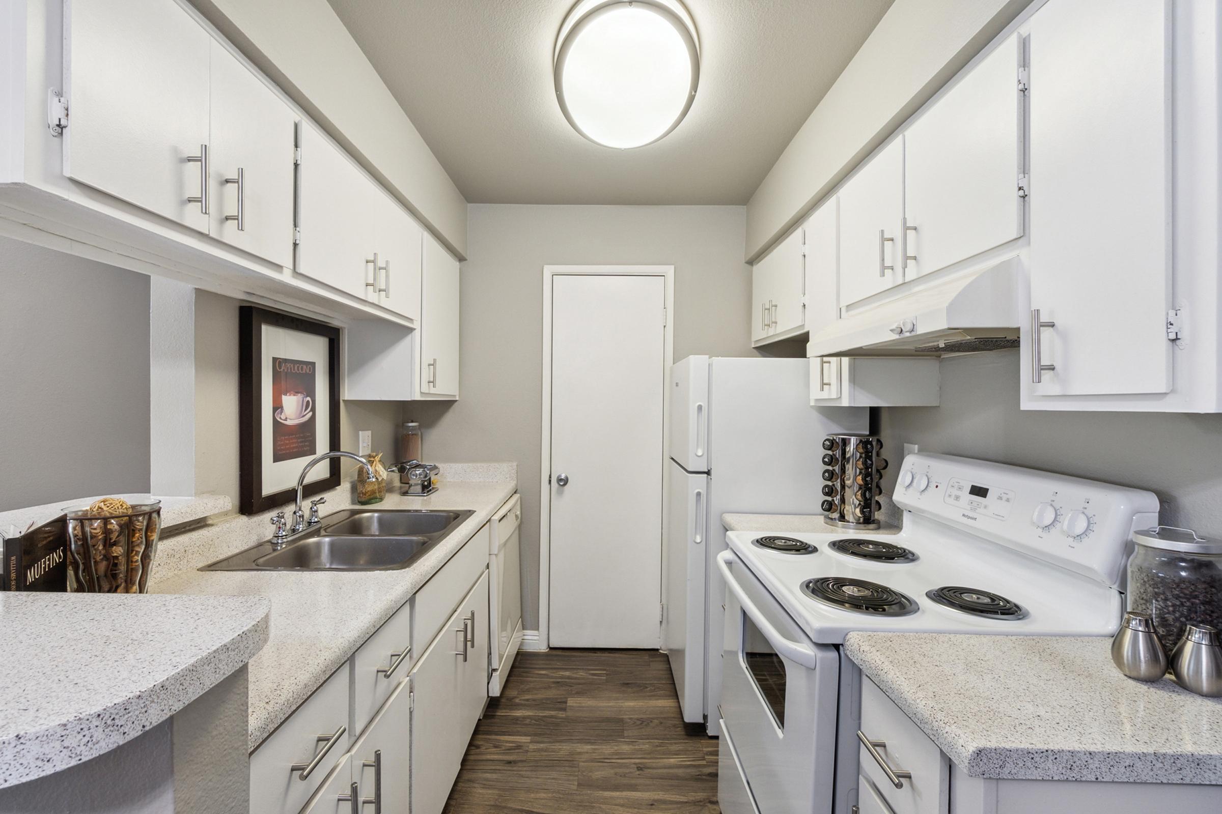 A modern kitchen featuring white cabinets, a double sink, a stove, and an oven.