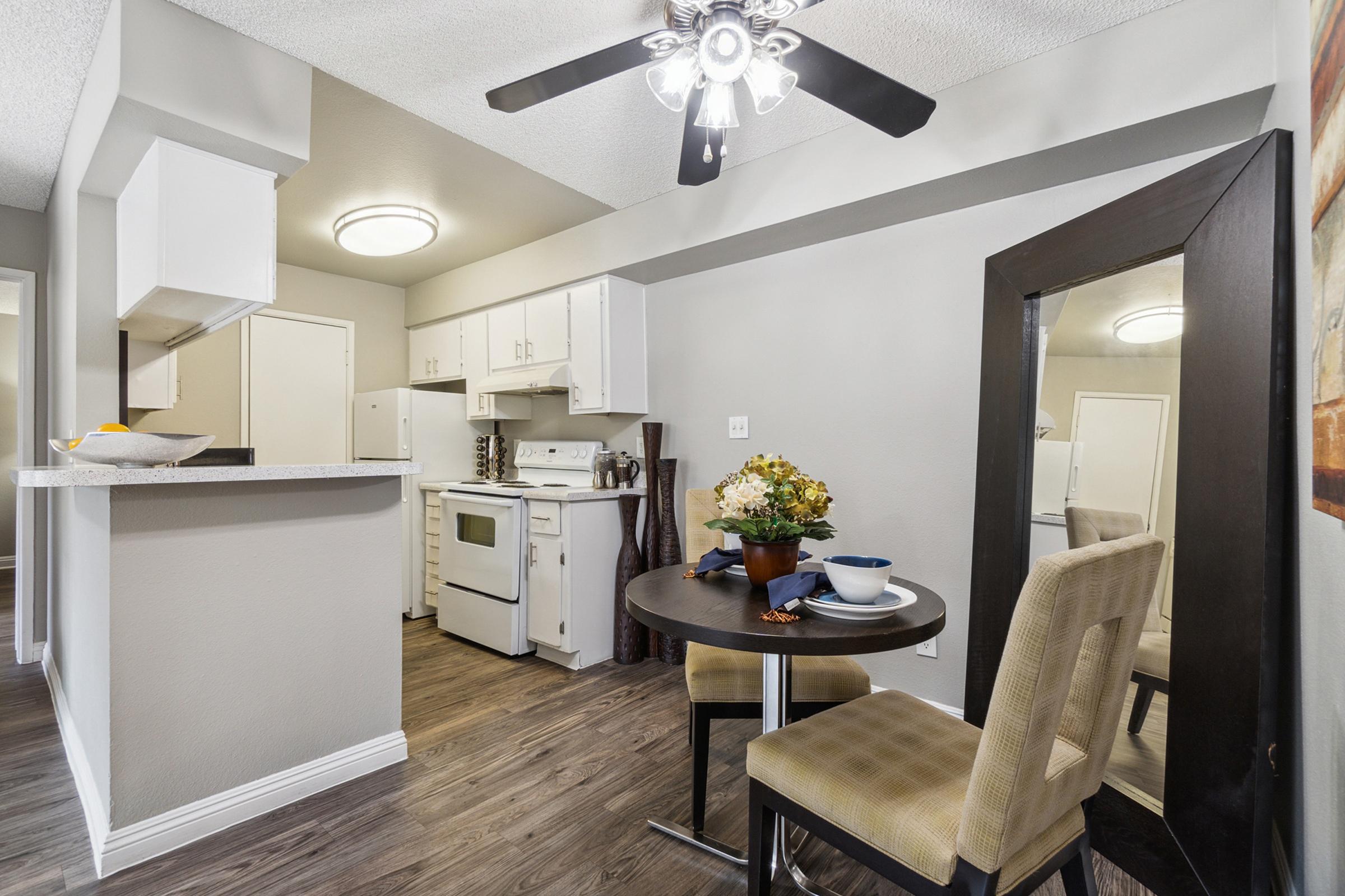 A modern kitchen and dining area featuring white cabinets, a stove, and a small round table with two chairs.
