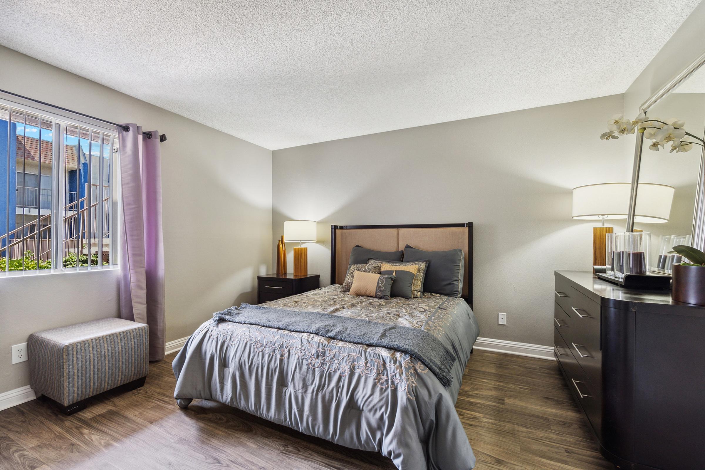 Cozy bedroom featuring a queen-sized bed with a decorative blanket, a nightstand with a lamp, and a dresser.