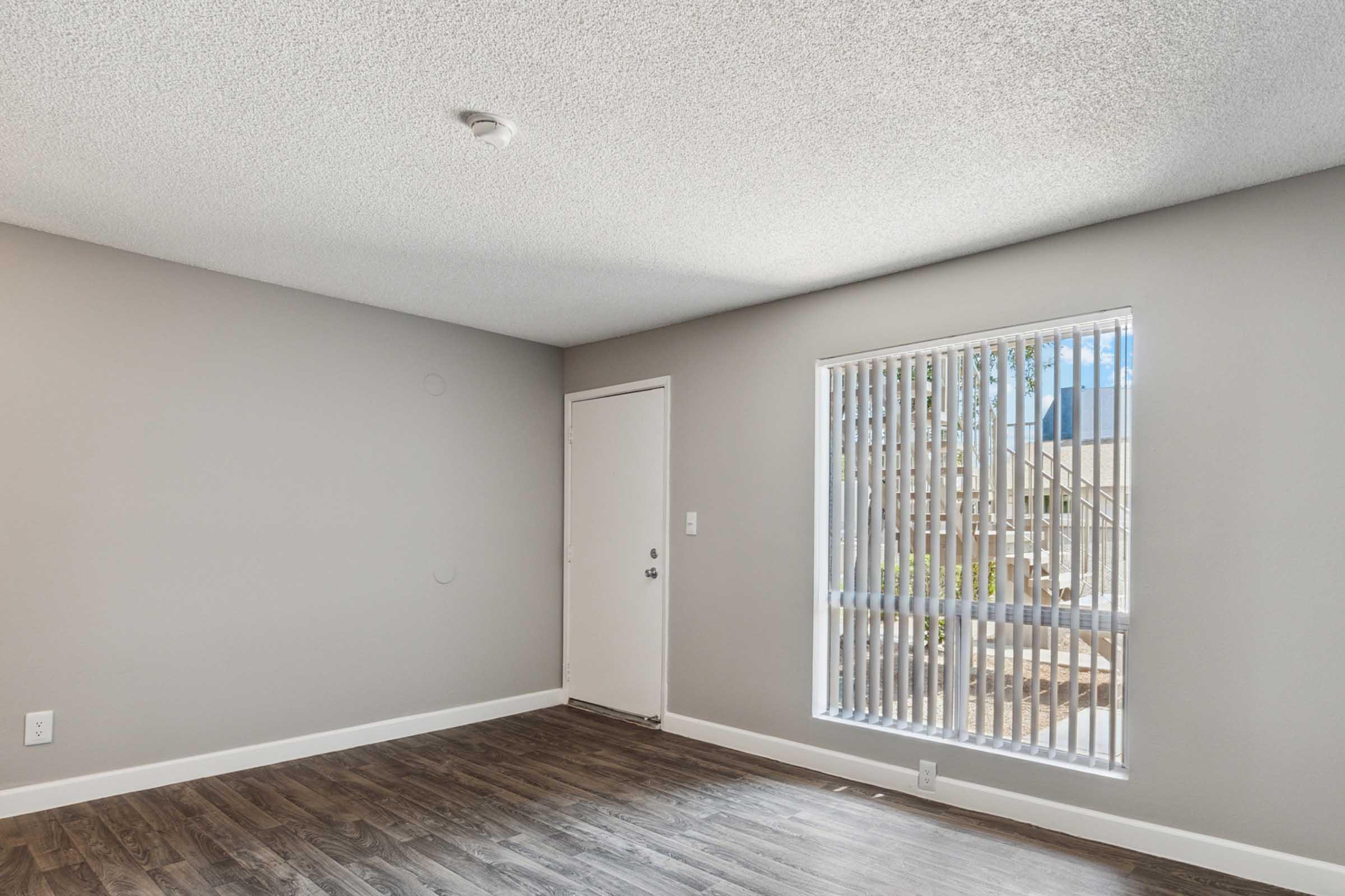 A well-lit room featuring a textured ceiling, light gray walls, and dark wood flooring.