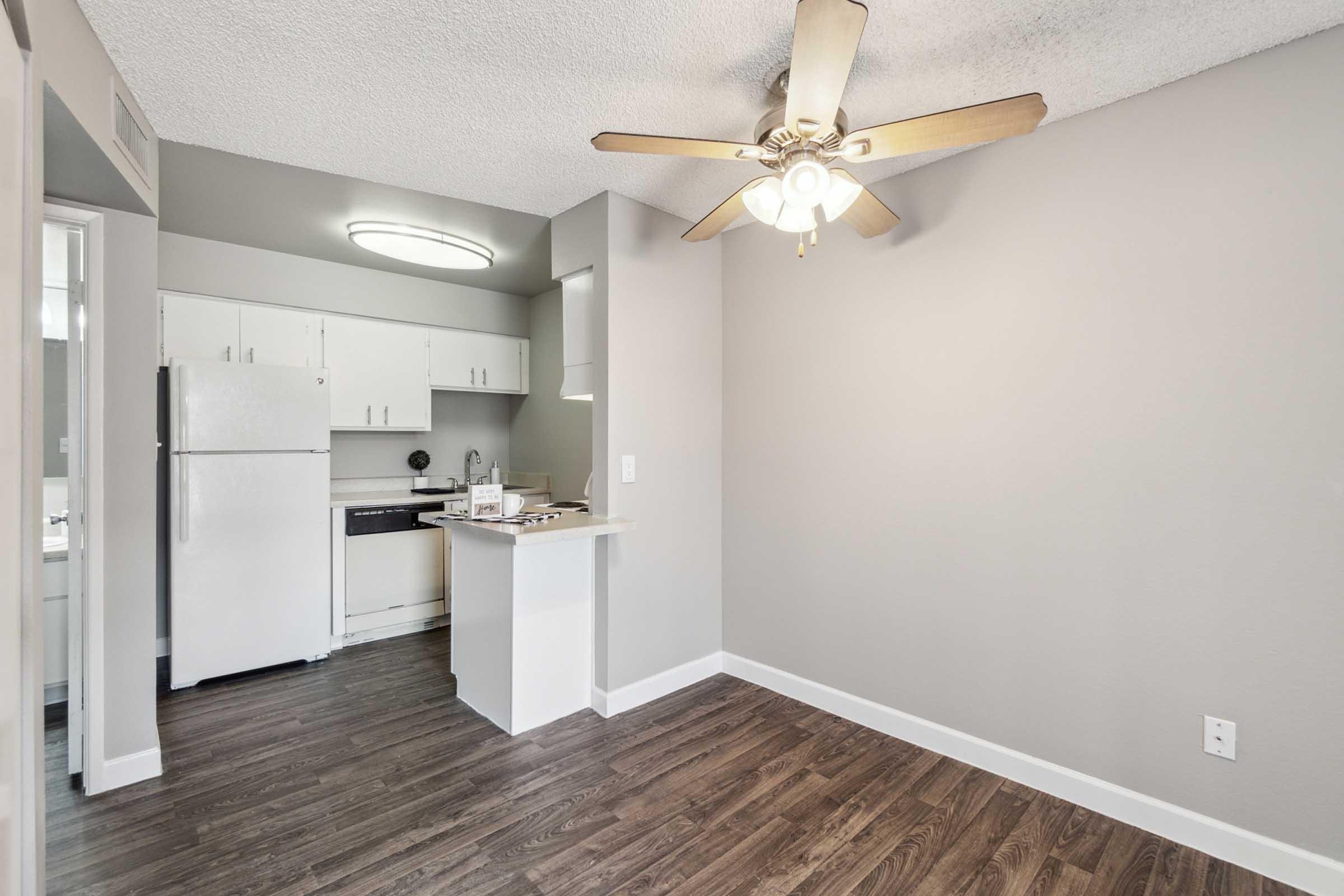 A modern kitchen area with a white refrigerator, black stove, and light-colored cabinets, featuring a ceiling fan with lights.