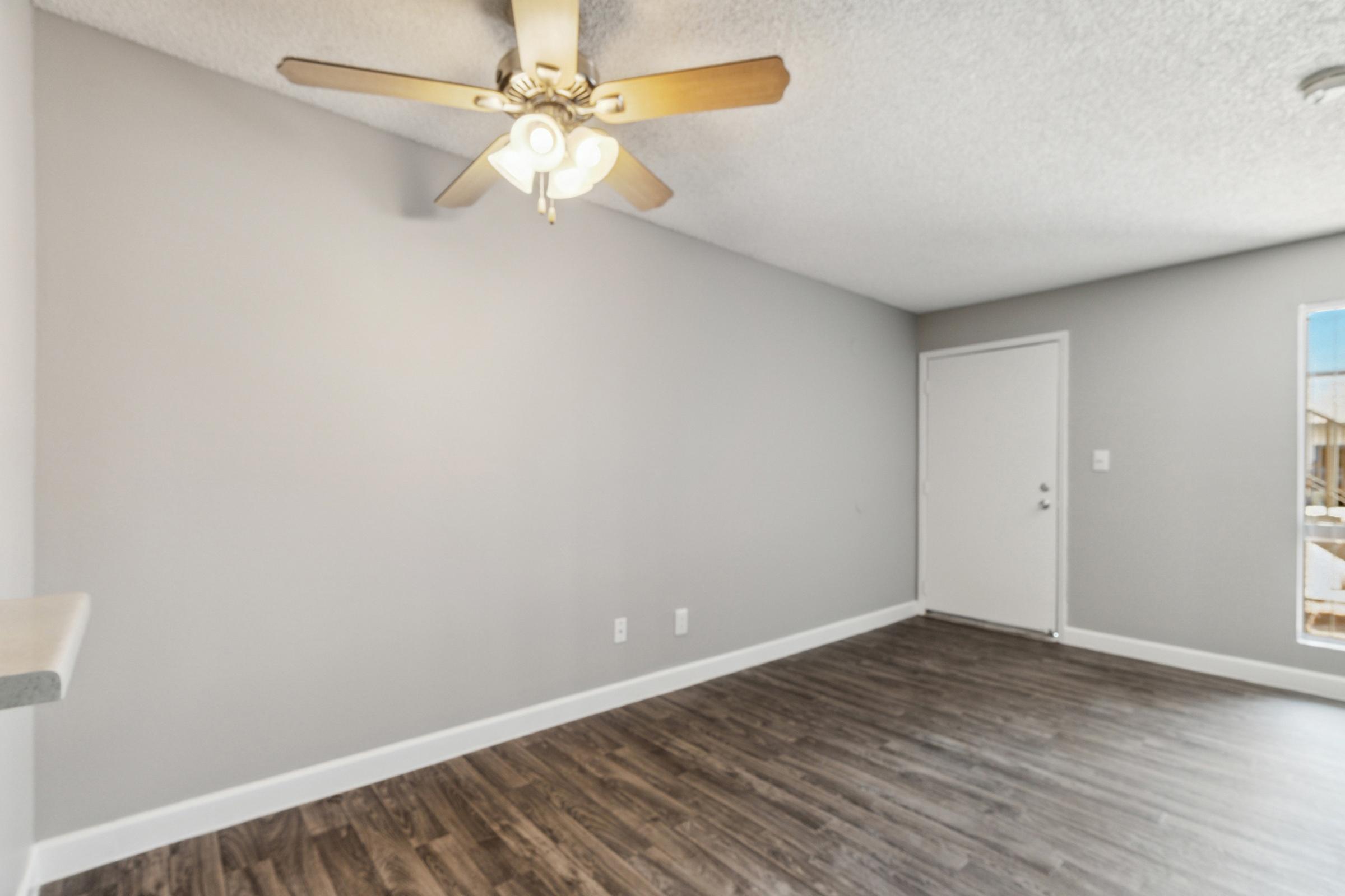 A well-lit room featuring a ceiling fan with four lights, neutral gray walls, and hardwood flooring.