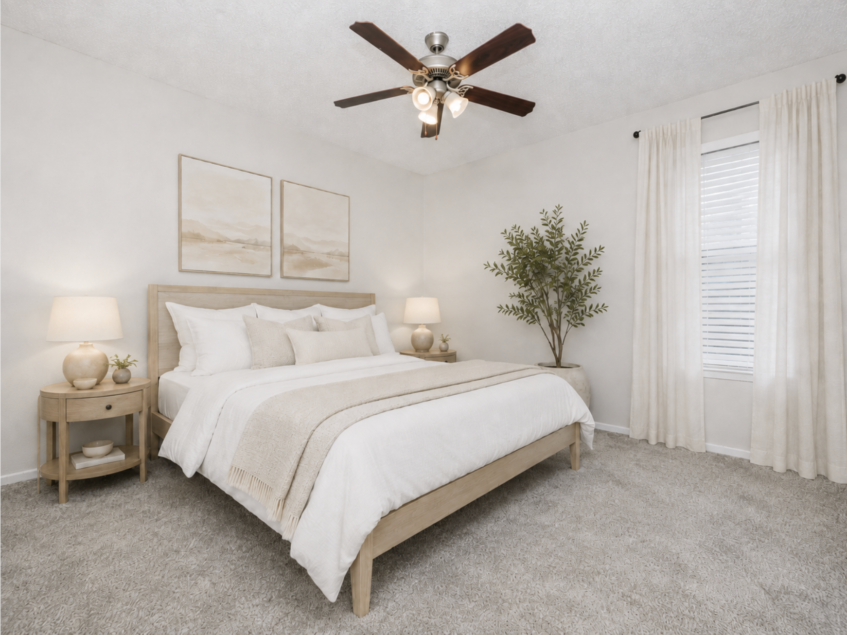 A cozy, minimalist bedroom featuring a large bed with white bedding and decorative pillows. Soft beige tones dominate the decor, with two bedside lamps and a potted plant. The room has a ceiling fan and a large window dressed with light curtains, creating a bright and inviting atmosphere.