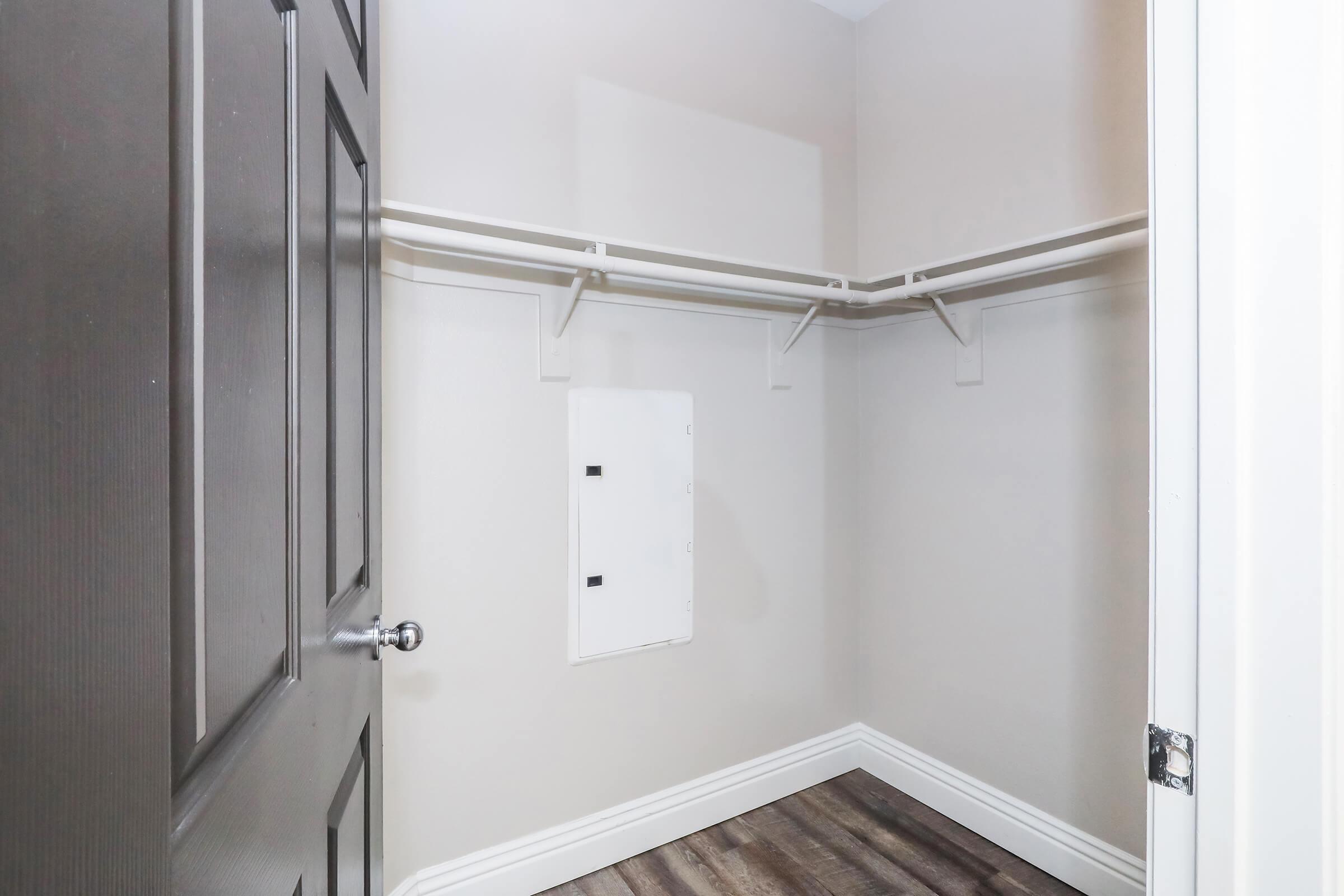 Empty room featuring a closet with a plain beige wall and a light gray door. The closet has a hanging rod and is equipped with a small electrical panel on the side. The flooring is a dark wood laminate, enhancing the modern aesthetic of the space.
