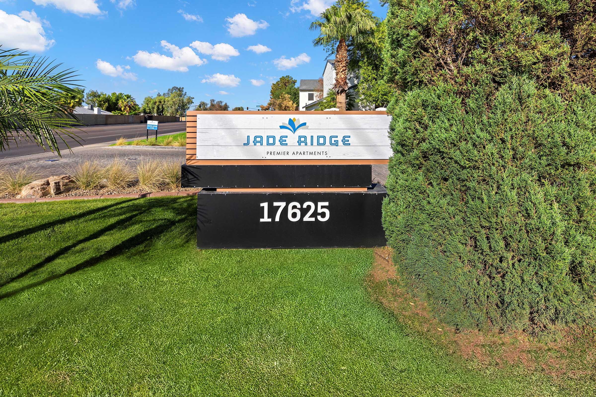 Sign for Jade Ridge Premier Apartments located at 17625, featuring modern design with blue and white lettering. Surrounded by well-maintained landscaping and palm trees, the sign is prominently displayed against a clear blue sky.