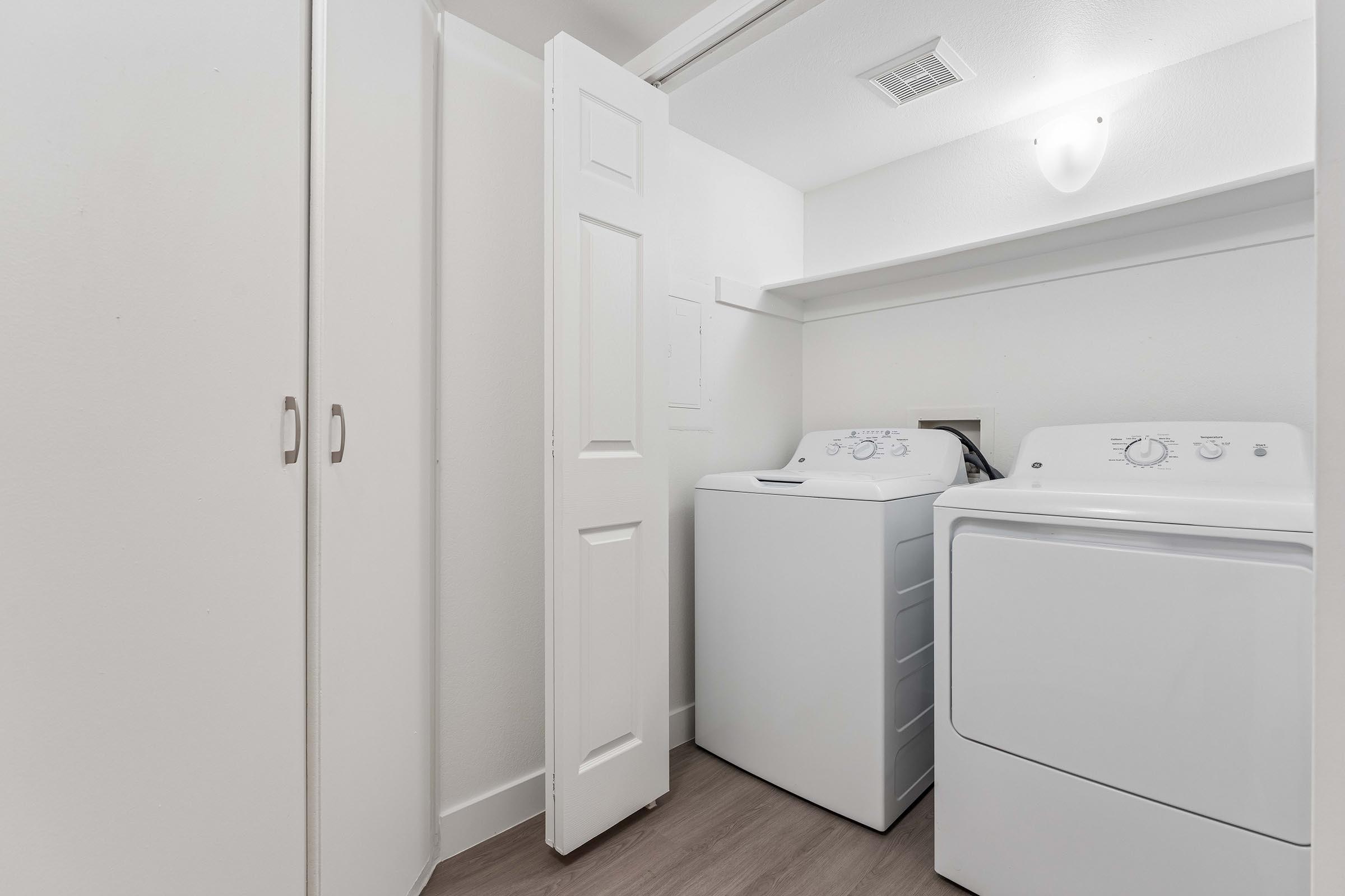 A small laundry room featuring a white washing machine and dryer side by side. The space includes light-colored walls, a ceiling light fixture, and a closet with white doors. There is minimal decor, creating a clean and functional environment for laundry tasks.