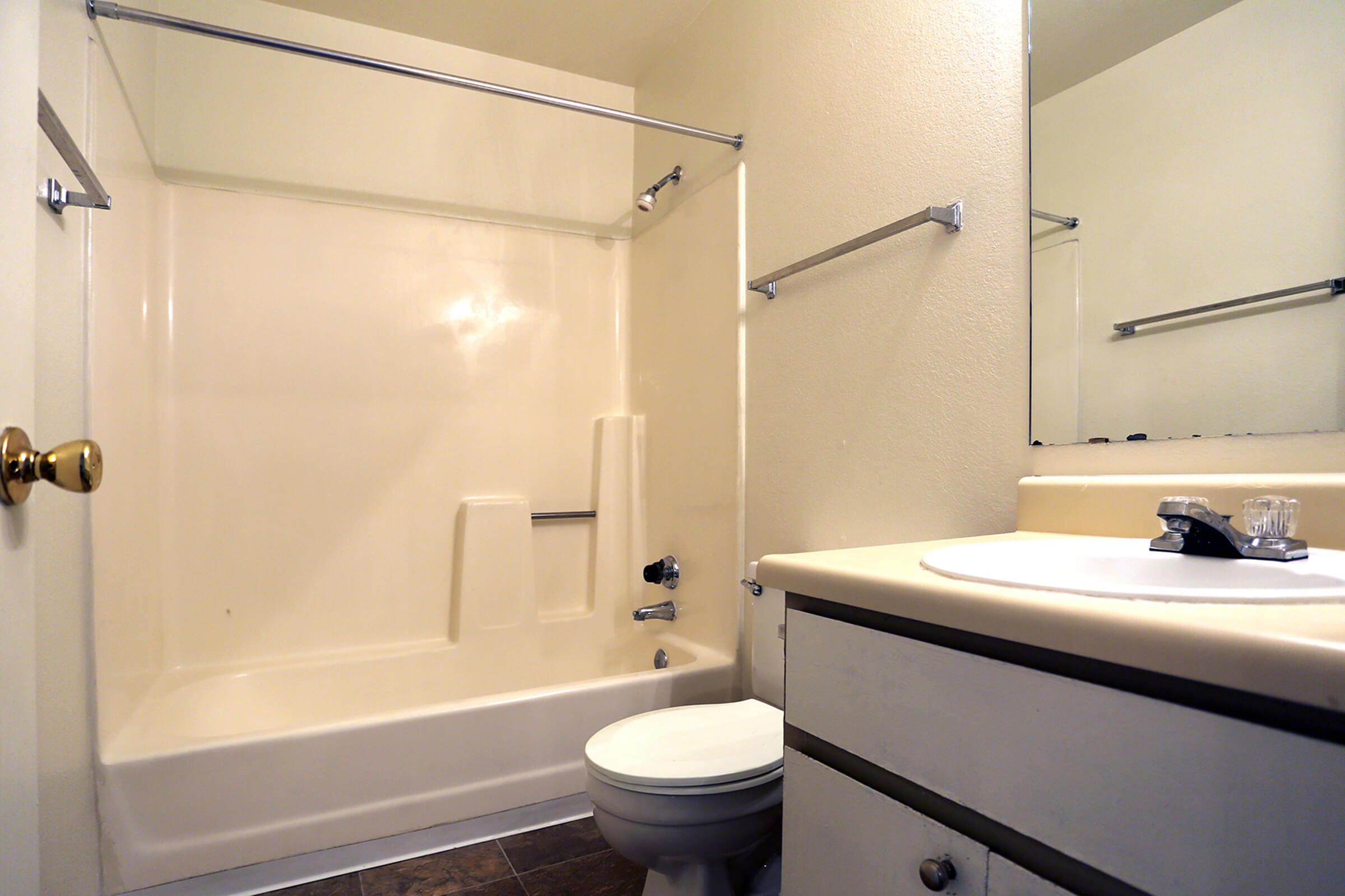 A simple bathroom featuring a shower and tub combination, a small vanity with a sink, and a toilet.
