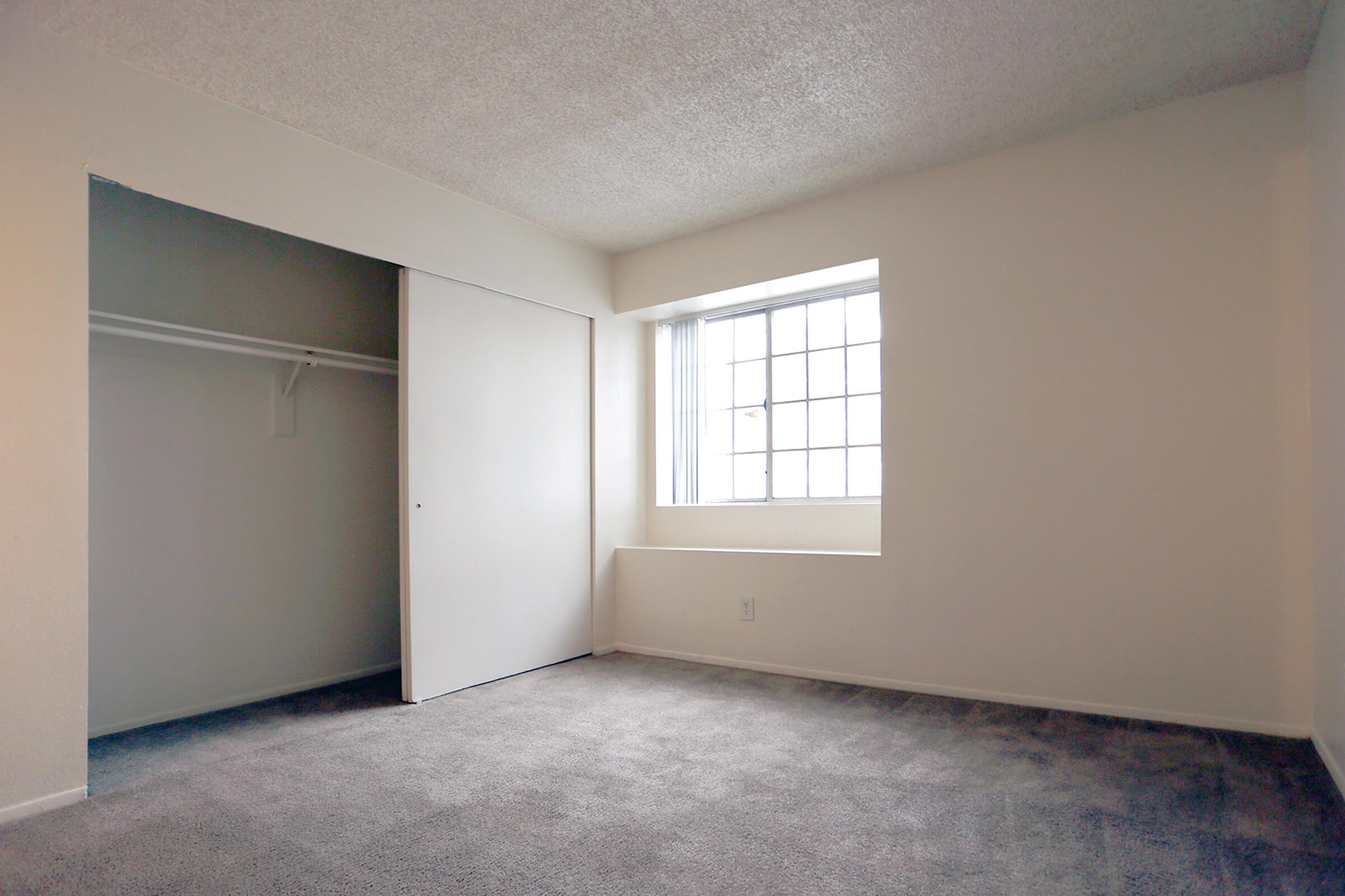 A spacious, empty bedroom featuring light-colored walls and gray carpet.