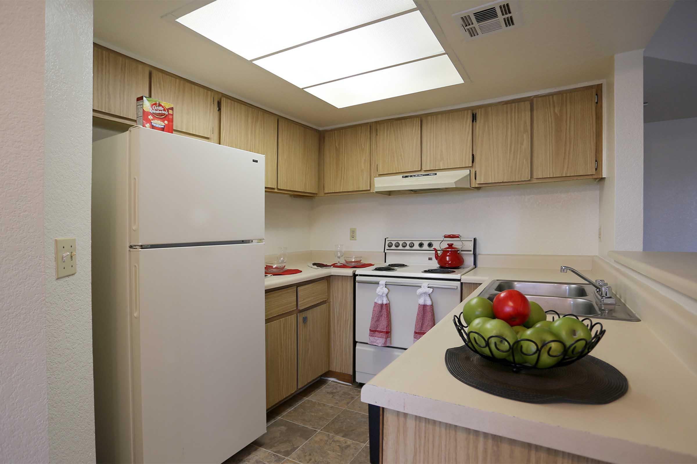 A compact kitchen featuring wooden cabinetry, a white refrigerator, a stove, and a sink.