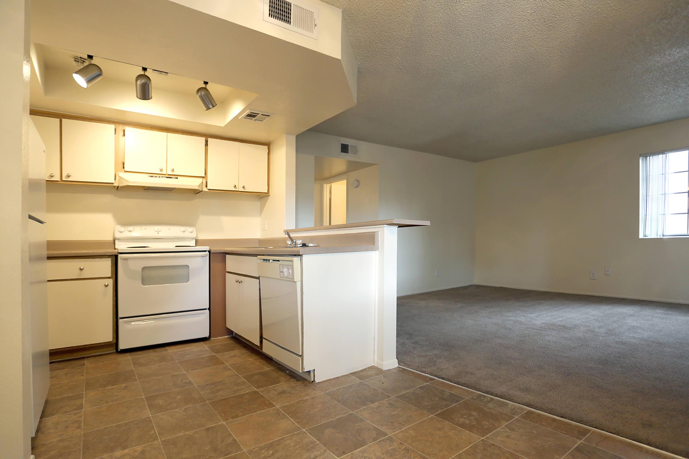 A well-lit kitchen featuring beige cabinets, a stove, and a dishwasher, with a tiled floor.