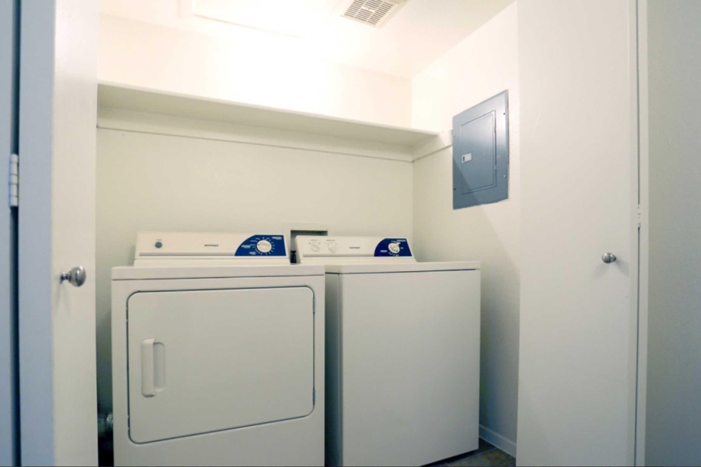A laundry room featuring a washing machine and dryer side by side on a light-colored floor, with shelves above for storage.