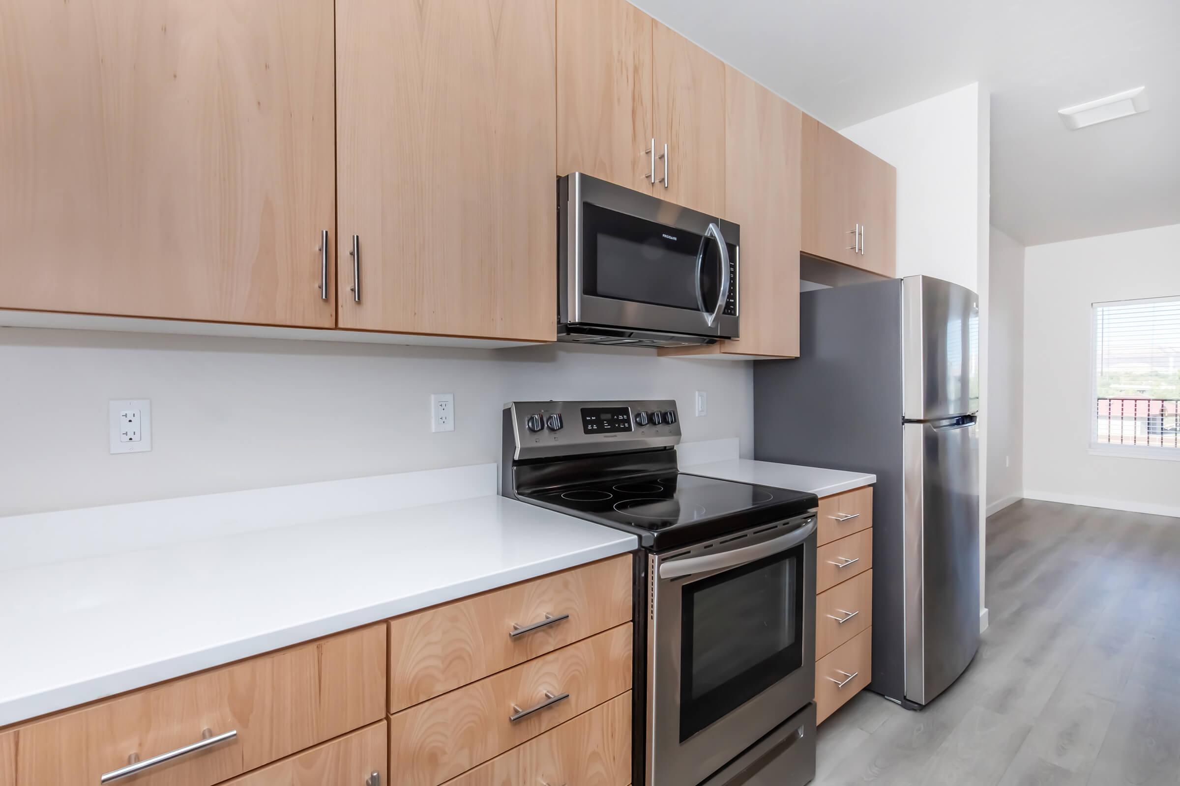 Modern kitchen featuring light wood cabinetry, stainless steel appliances including a microwave and refrigerator, and a black stove. The countertops are white, and there is a window providing natural light, highlighting the contemporary design.