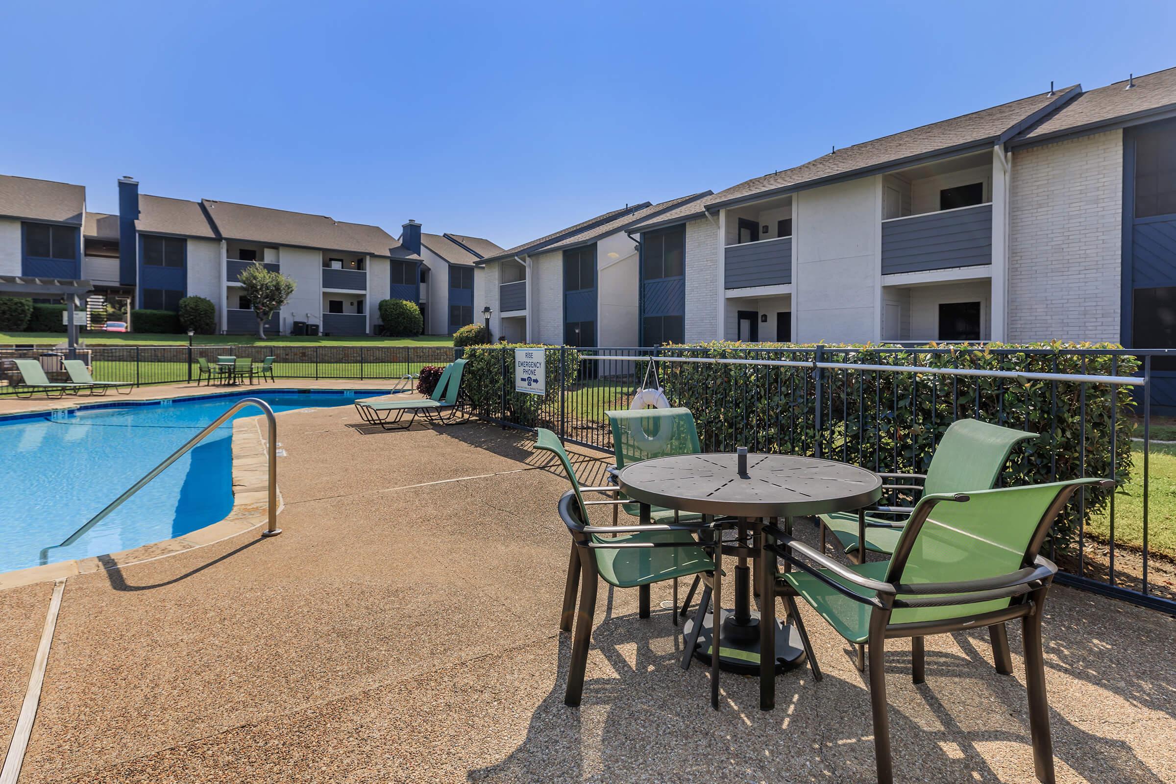 A pool, loungers and table with seating within the Rise Oak Creek apartment community.