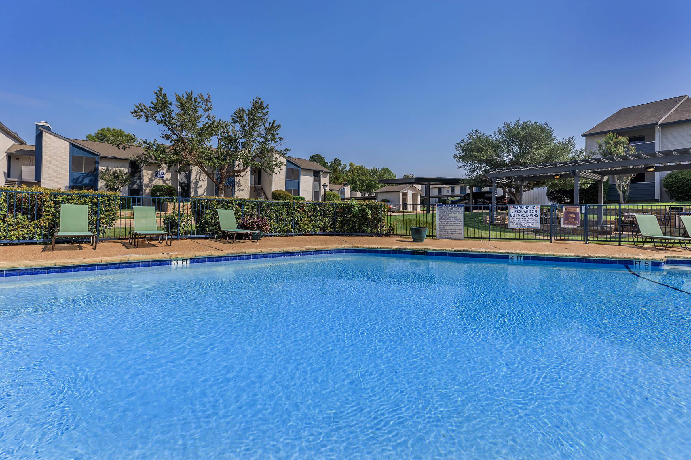 A dazzling pool surrounded by foliage and the Rise Oak Creek apartments.