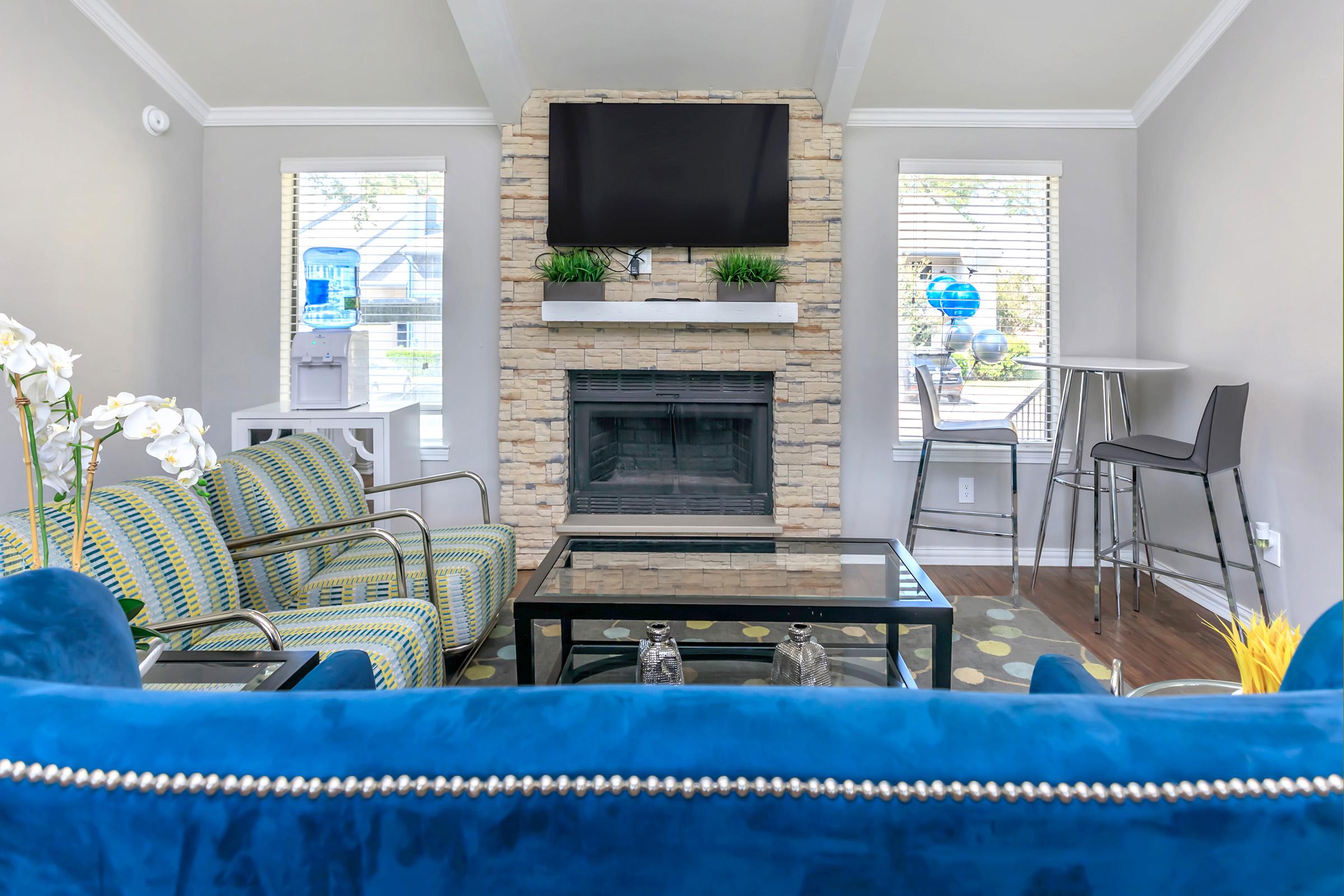 A living room with a blue couch, two windows and a fireplace at Rise Oak Creek.