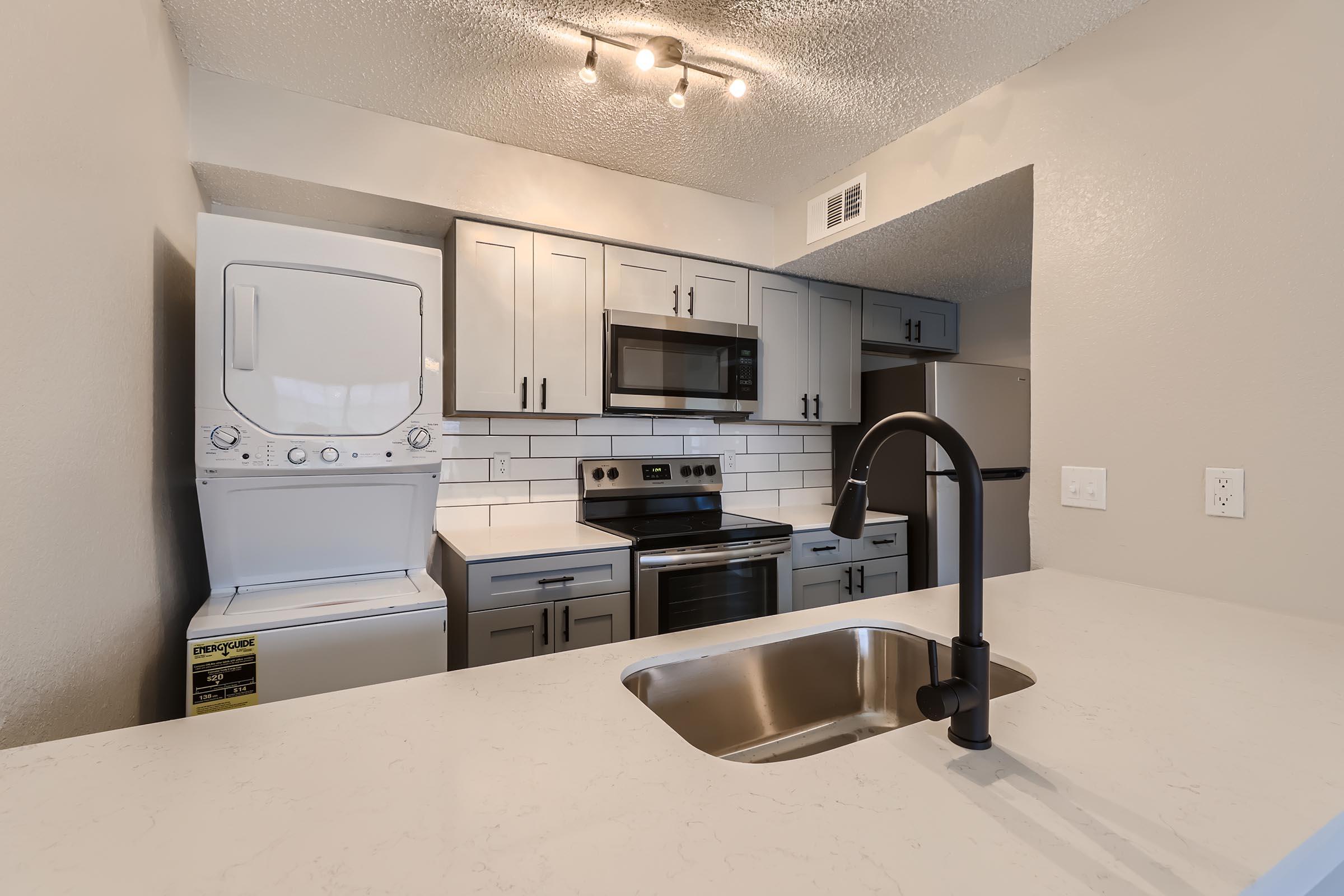 A kitchen with a washer and dryer, shaker cabinets, and stainless steel appliances.