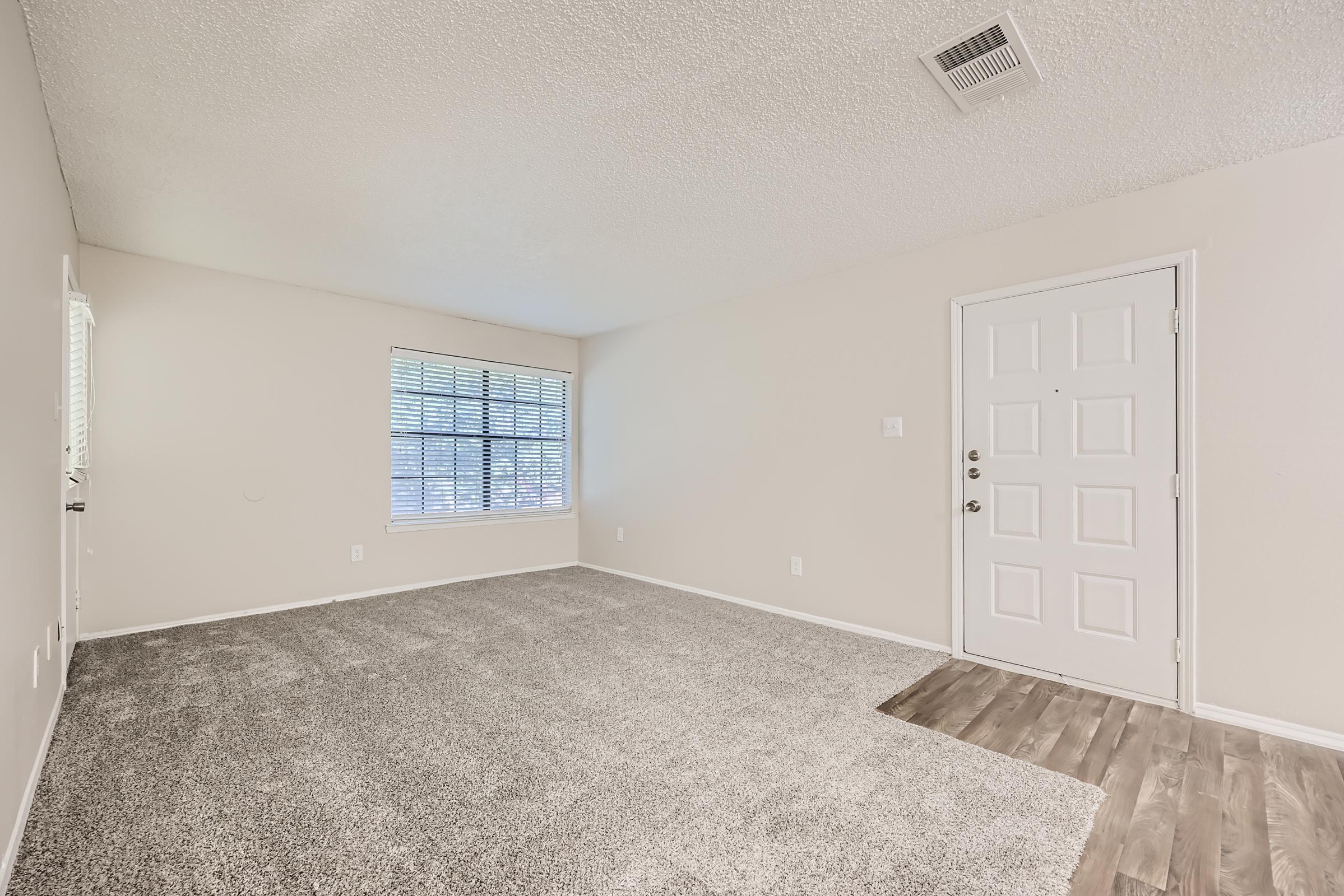 A carpeted living room at Rise Oak Creek near the dining area with wood-style flooring.