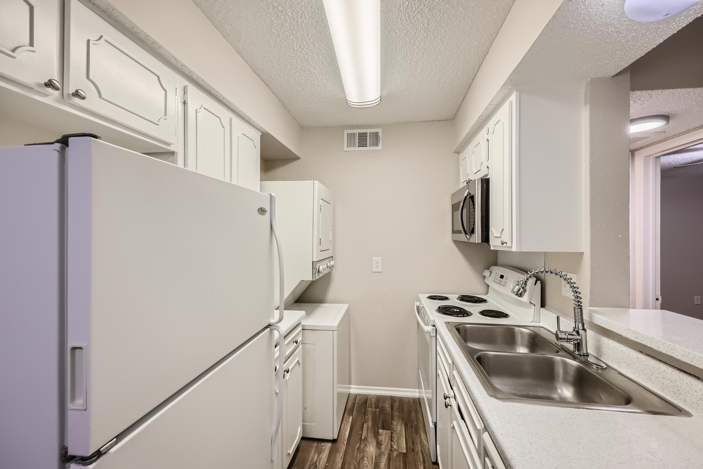 A galley kitchen with white cupboards, white appliances and a view to the living area at Rise Oak Creek.