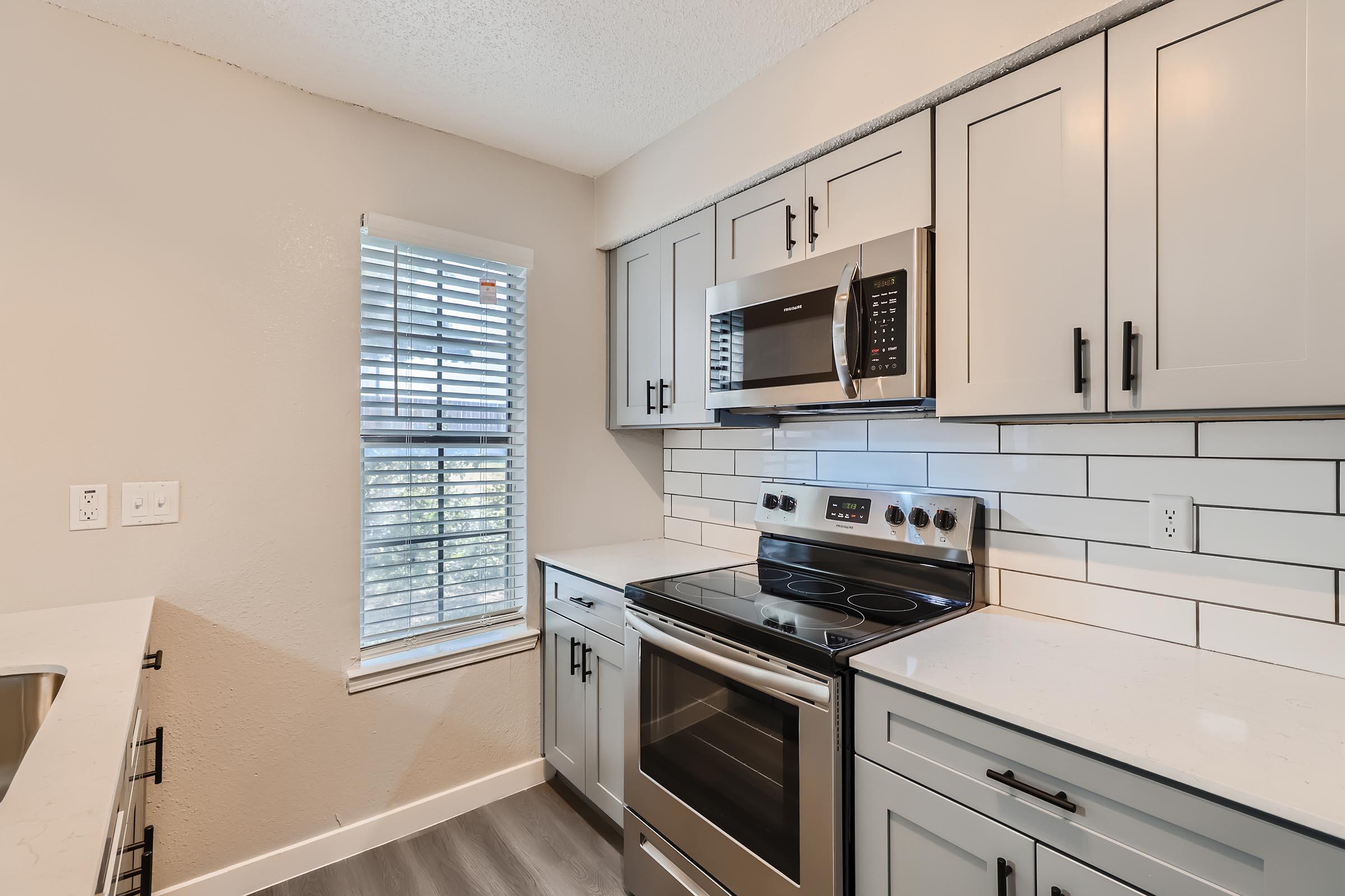 An apartment kitchen with grey shaker cabinets and a window at Rise Oak Creek.