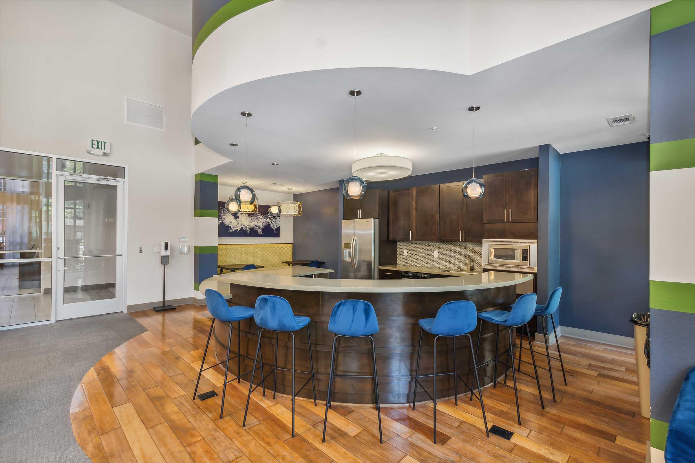 A modern kitchen with a large curved island featuring bar stools, sleek dark cabinetry, and stainless steel appliances.