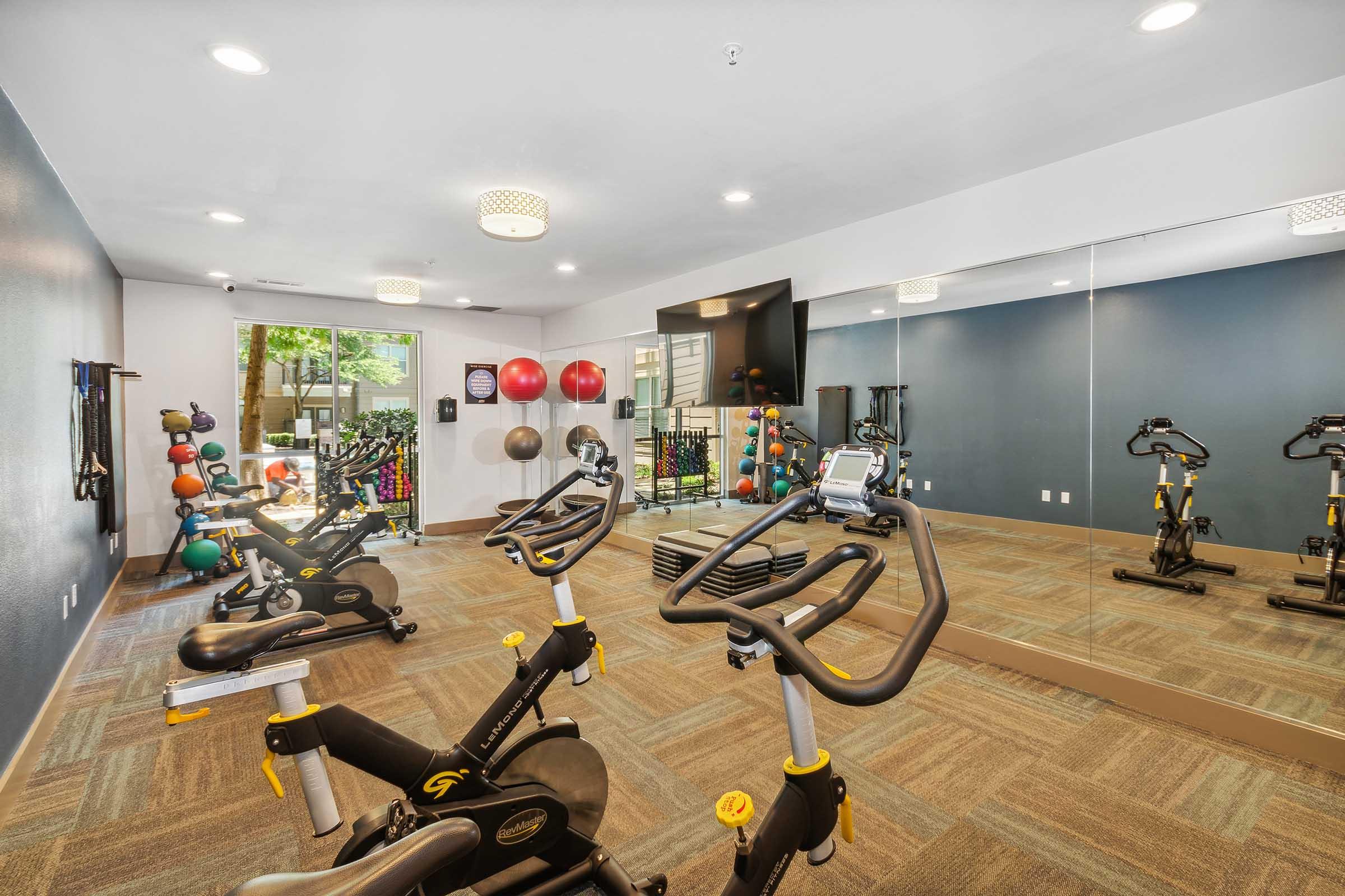A modern fitness room featuring exercise bikes, weights, and exercise balls.