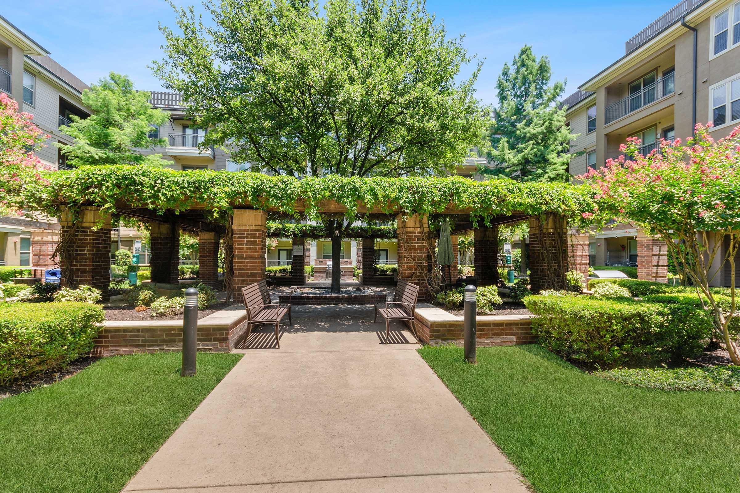 A serene outdoor courtyard featuring a stone path, benches, and lush greenery.