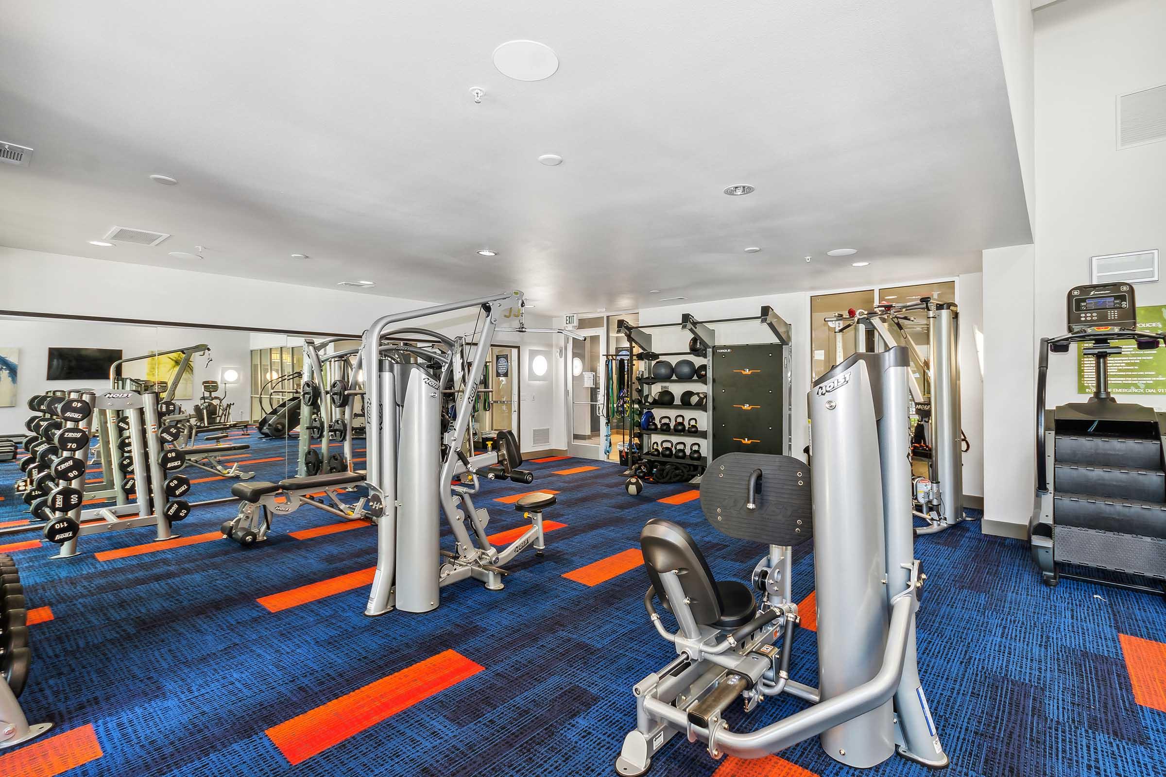 A modern gym interior featuring various workout equipment, including weight machines, free weights, and cardio machines.