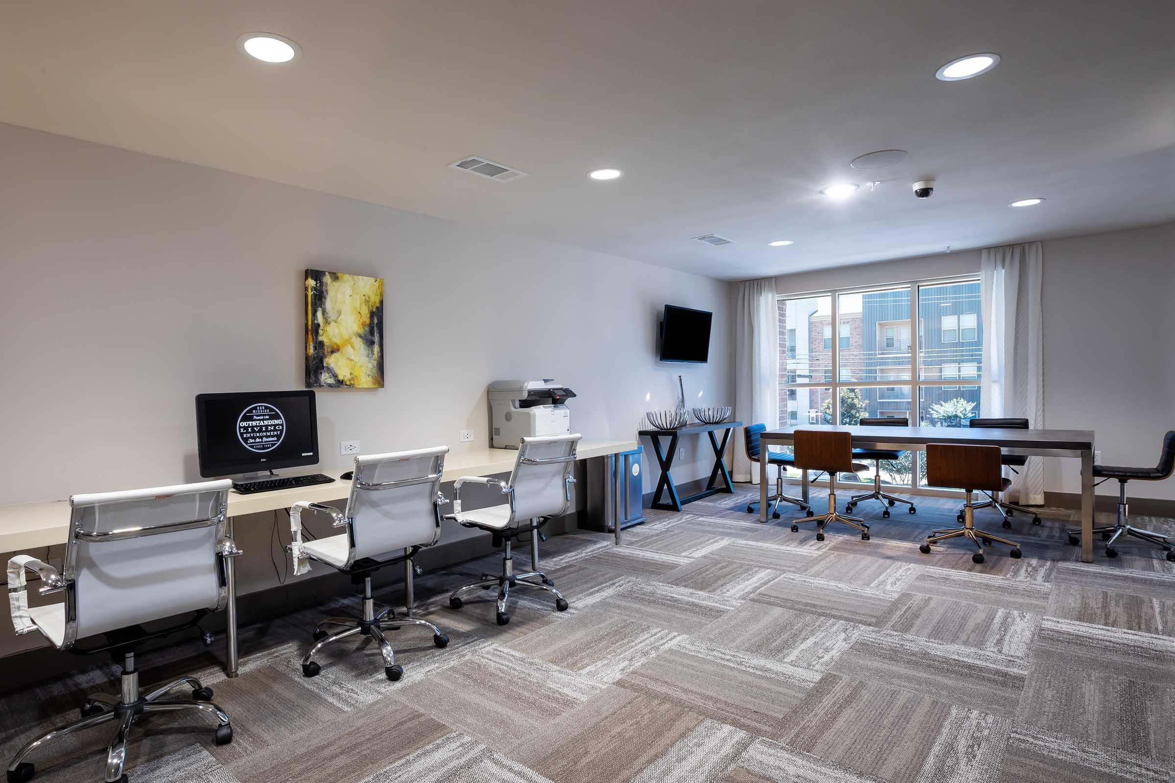 A modern office space featuring two workstations with ergonomic chairs, a printer, and a large window letting in natural light.