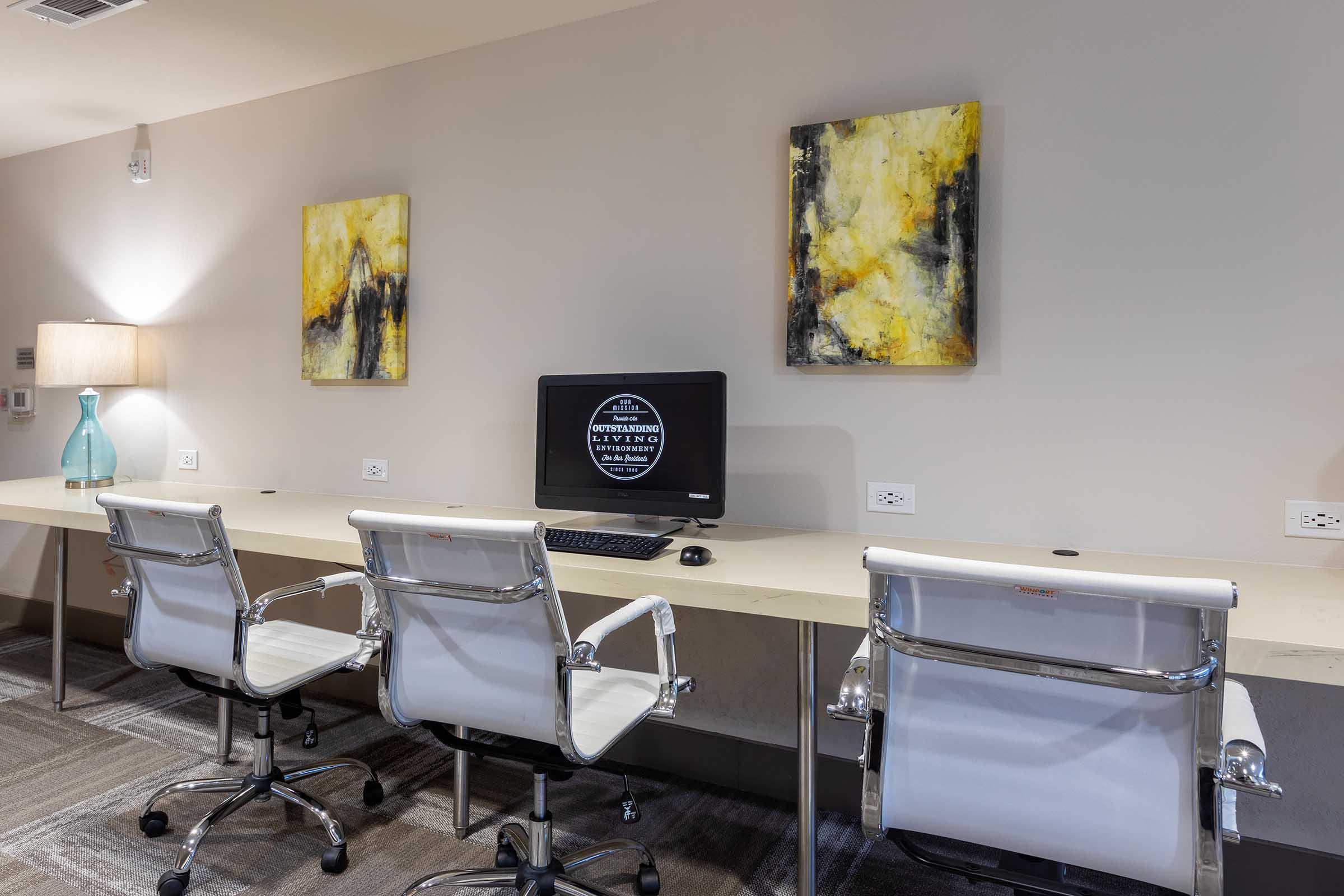 A modern office space featuring a long desk with two white ergonomic chairs, a computer on the desk, and a lamp.