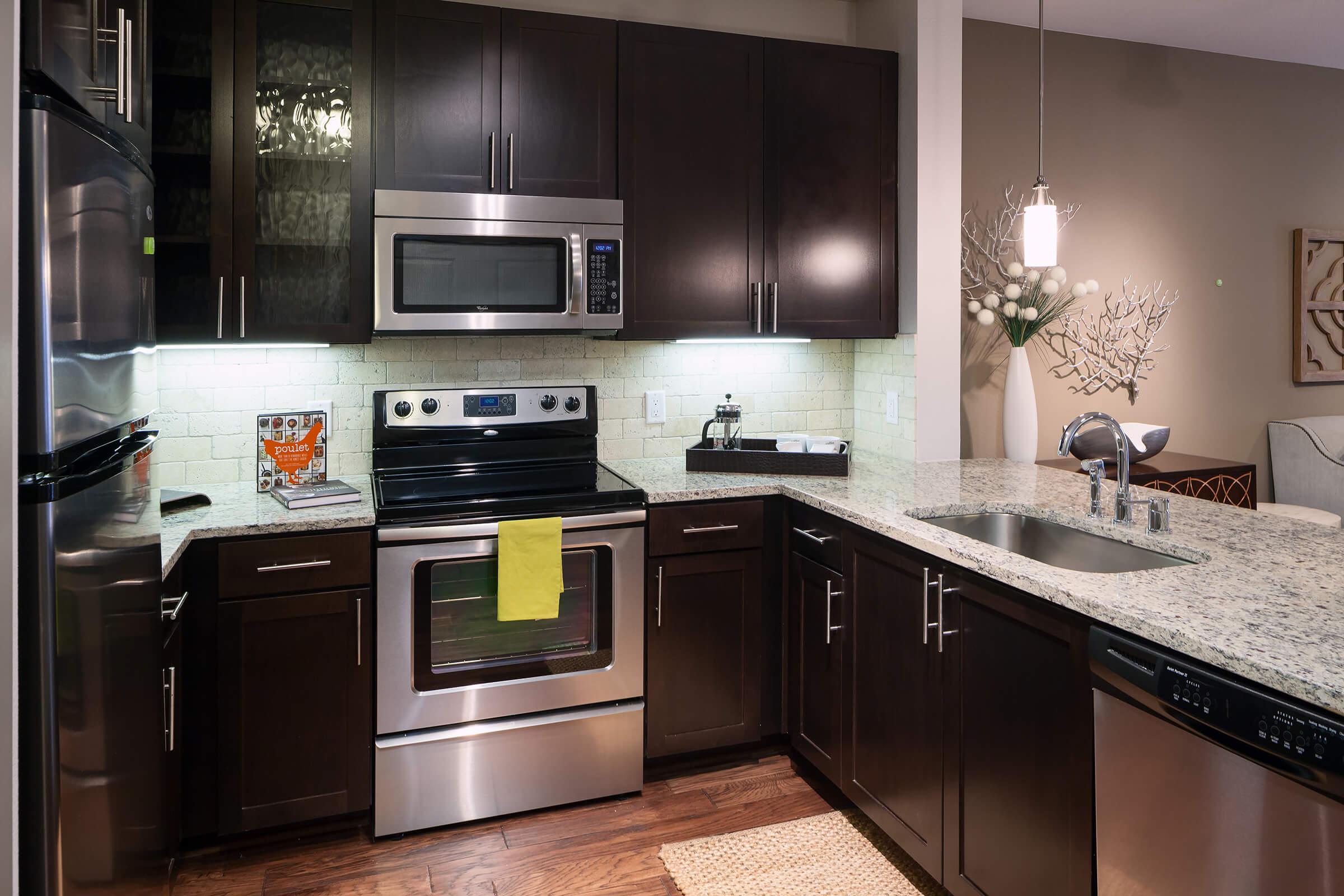 Modern kitchen featuring dark wood cabinets, stainless steel appliances including an oven, microwave, and dishwasher.