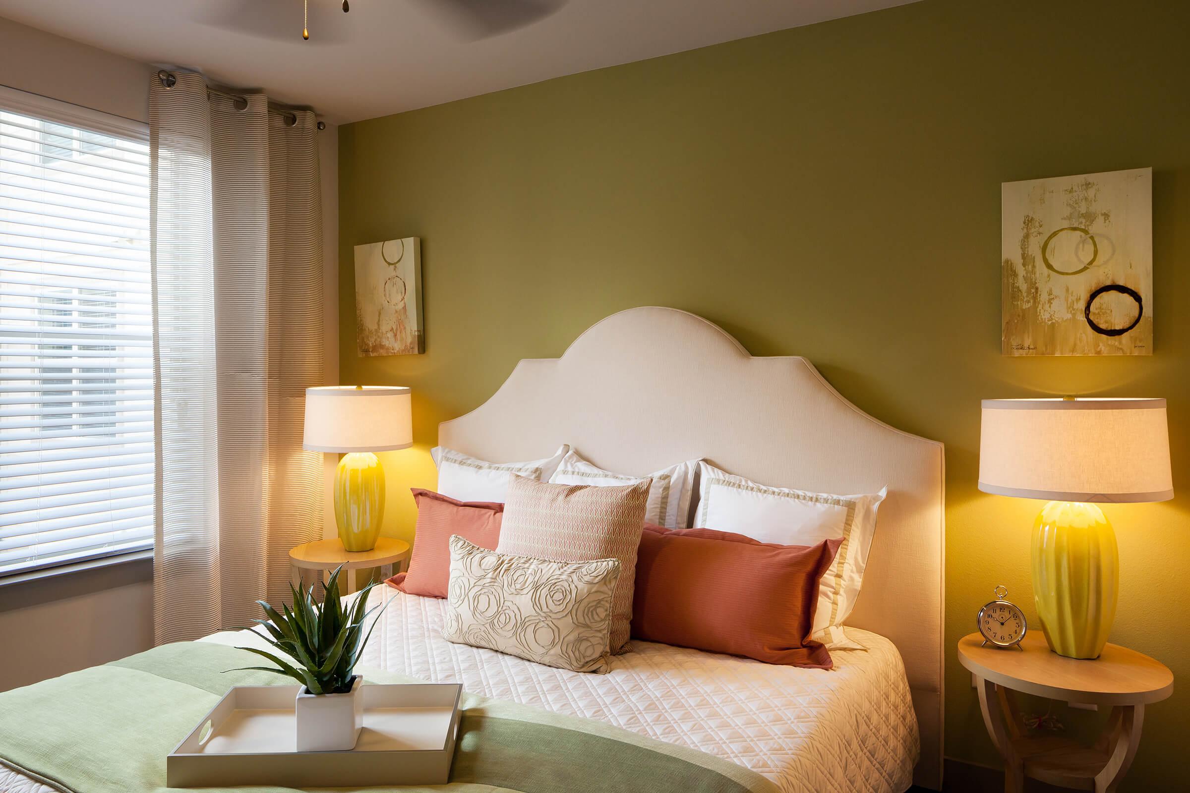 A cozy bedroom featuring a light green accent wall, a plush white bed with decorative pillows, and a quilted blanket.
