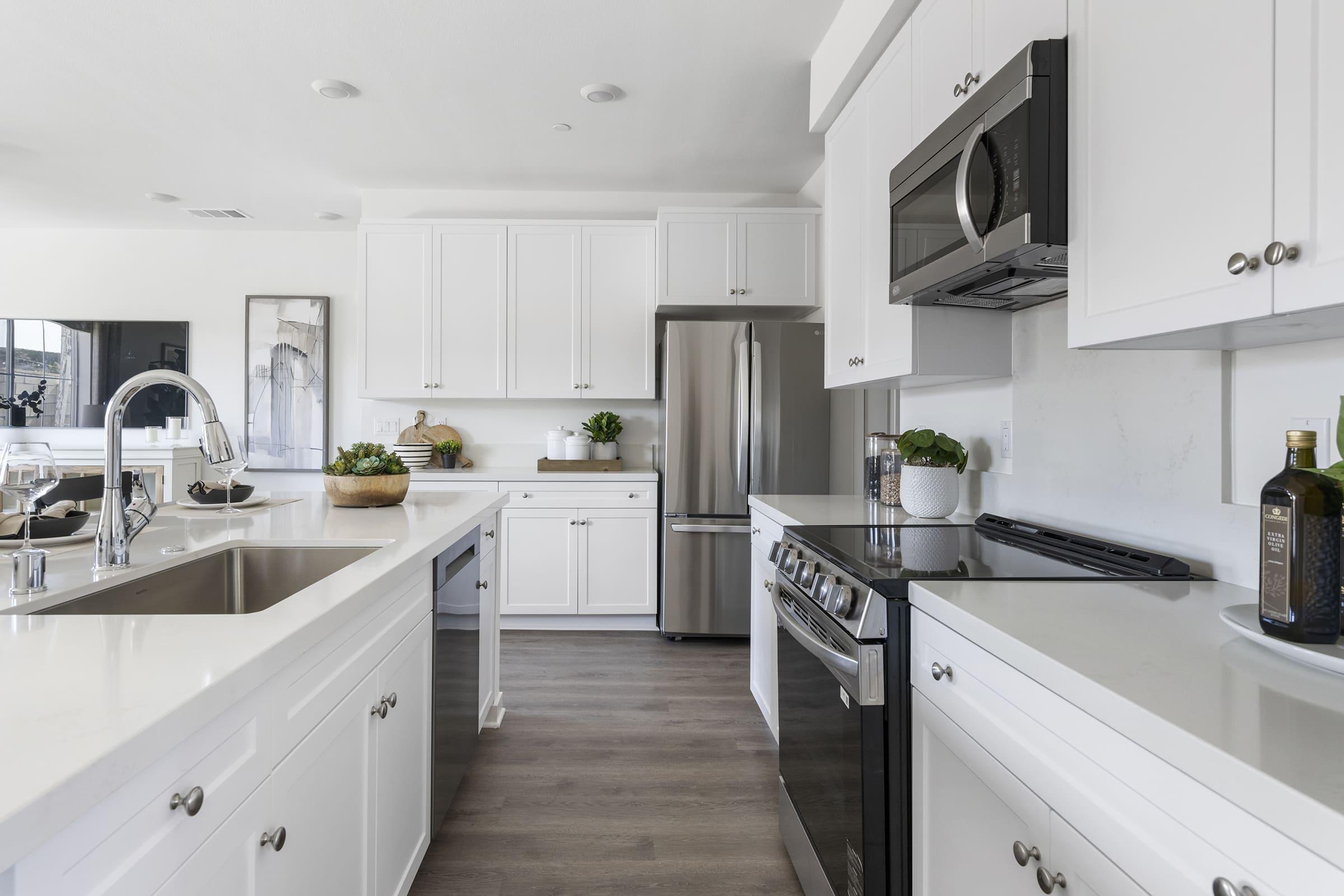 Bright and modern kitchen featuring white cabinets, stainless steel appliances, and a sleek countertop. The space is open and spacious, with a large sink, a built-in microwave, and decorative plants. Natural light floods the area, highlighting the contemporary design.
