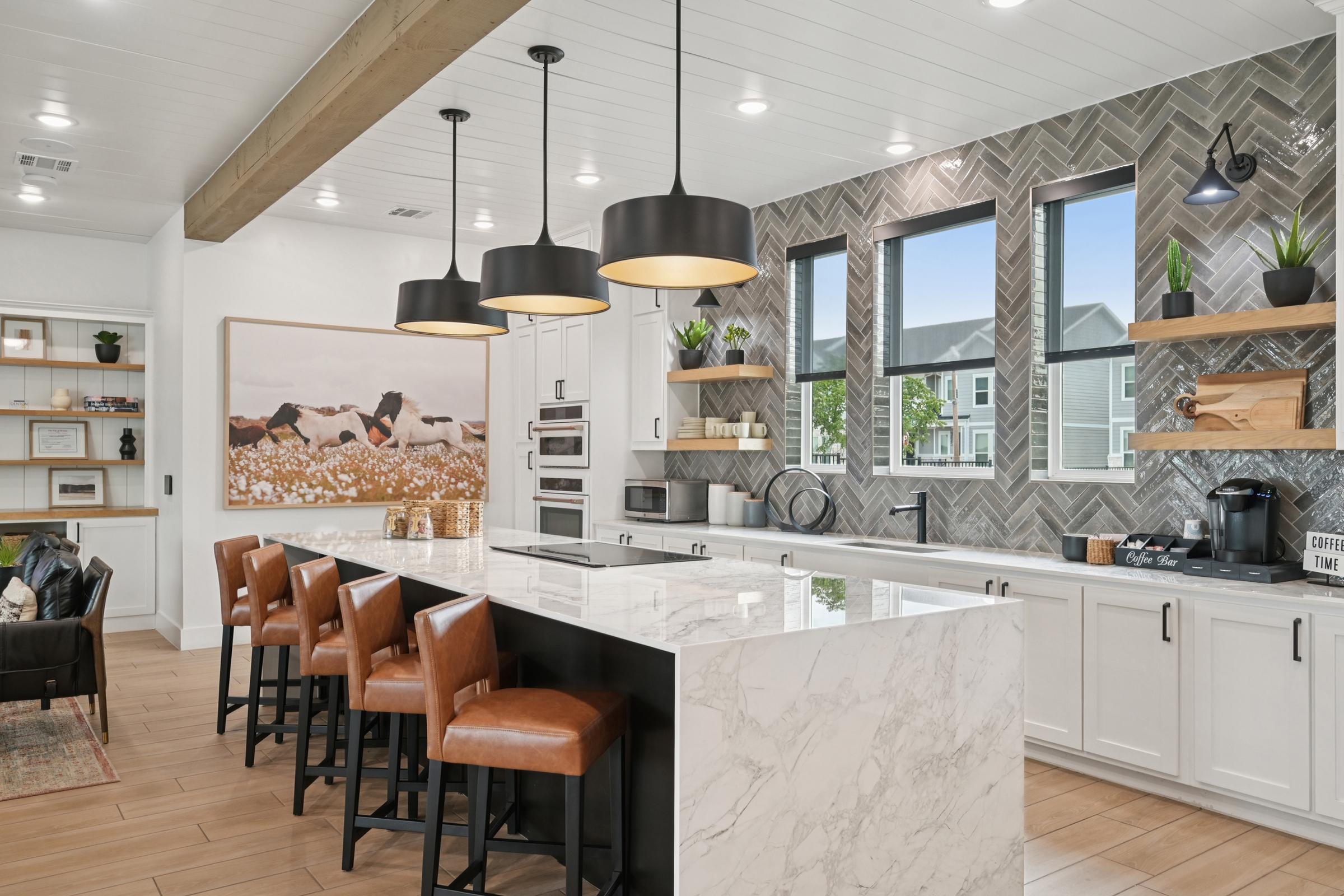 Spacious modern kitchen featuring a large marble island with bar seating, contemporary light fixtures, and stylish cabinetry. The backsplash is designed with herringbone tiles, complemented by open shelves displaying plants and decorative items, while large windows provide natural light.