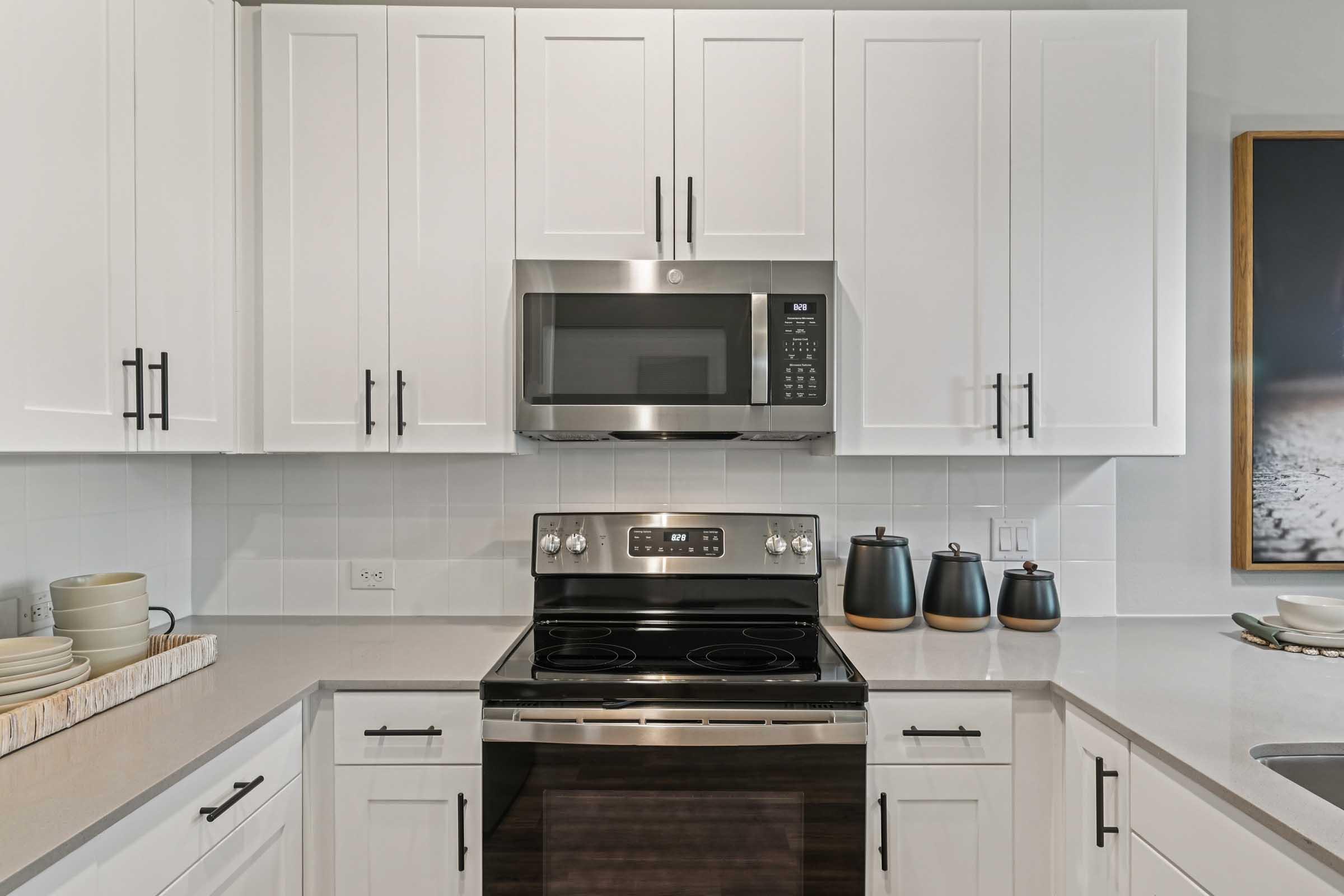Modern kitchen featuring white cabinets, stainless steel appliances, and a sleek countertop. An electric stove and built-in microwave are visible, along with decorative bowls and containers on the counter. A framed artwork is hung on the wall, adding a touch of elegance to the space.