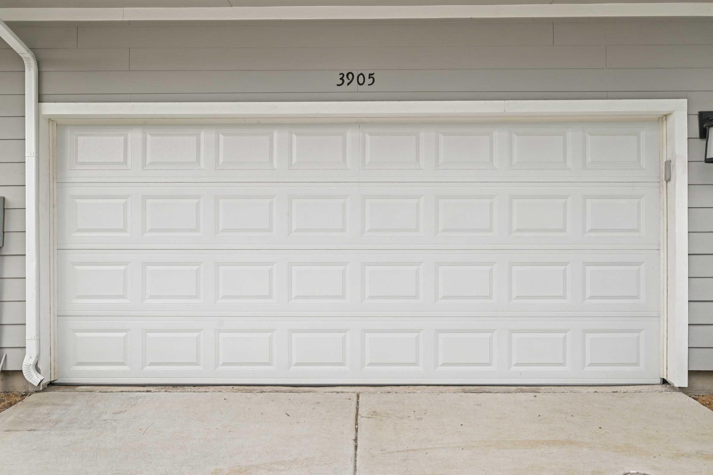 A white garage door with a textured surface, featuring rectangular panels, located at the property numbered 3905. The surrounding area includes a concrete driveway and light-colored siding of the house.