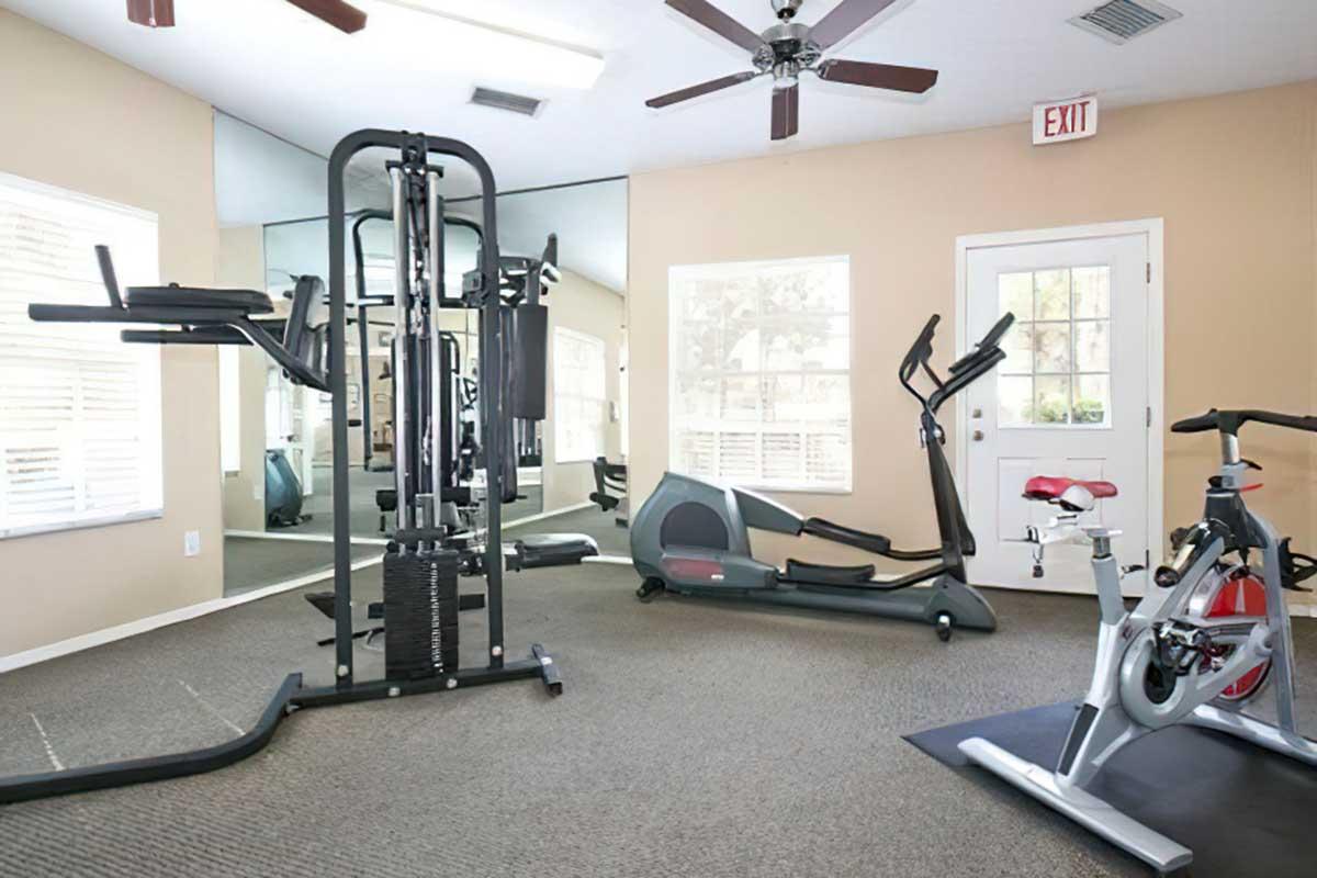 A well-lit fitness room featuring various exercise equipment including a multi-gym machine, an elliptical trainer, and a stationary bike.