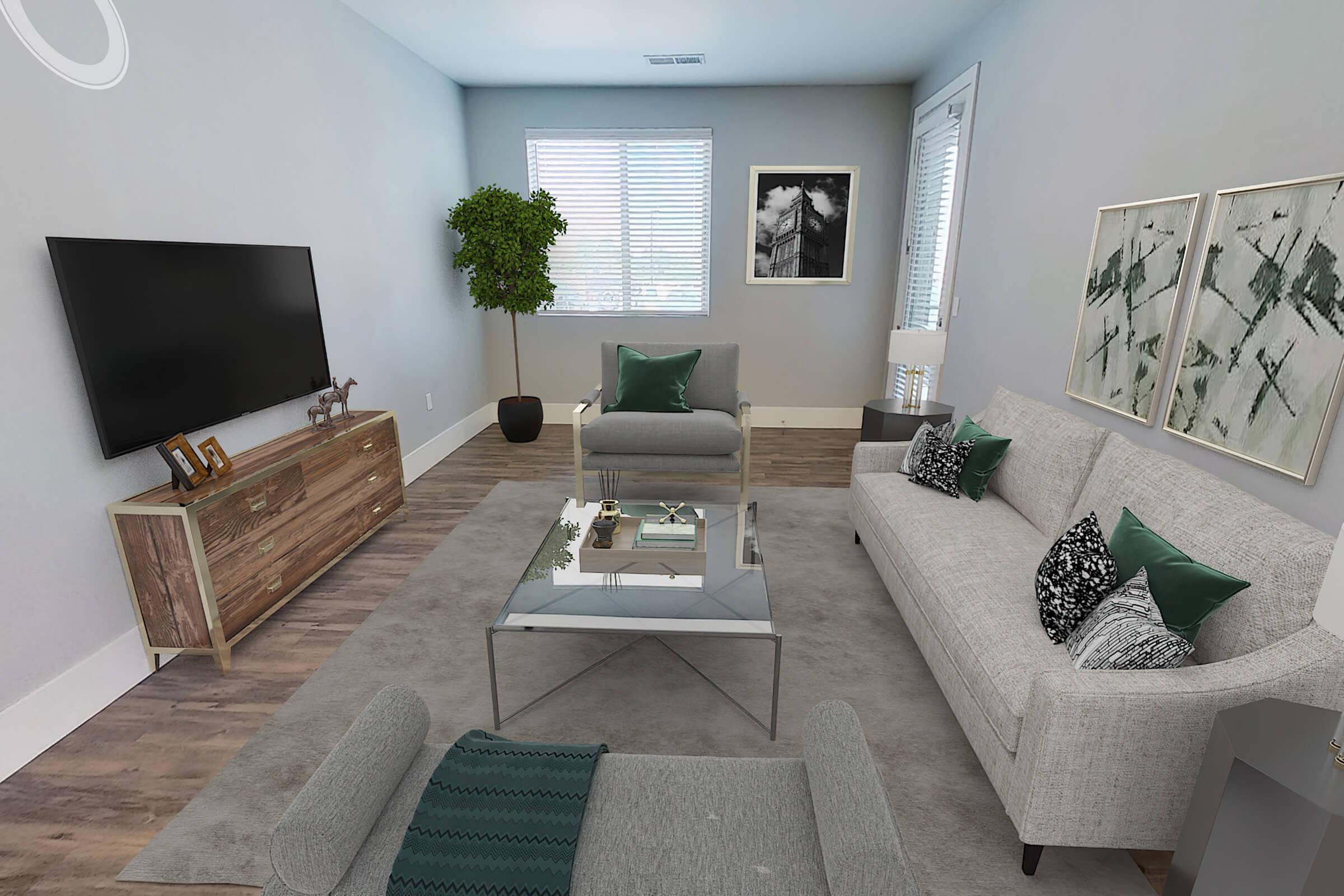 A modern living room featuring a light gray sofa with green cushions, two armchairs, a glass coffee table, and a wooden TV stand. The room includes a large television, a decorative plant in the corner, and abstract wall art. Natural light enters through window blinds, creating a bright and airy atmosphere.